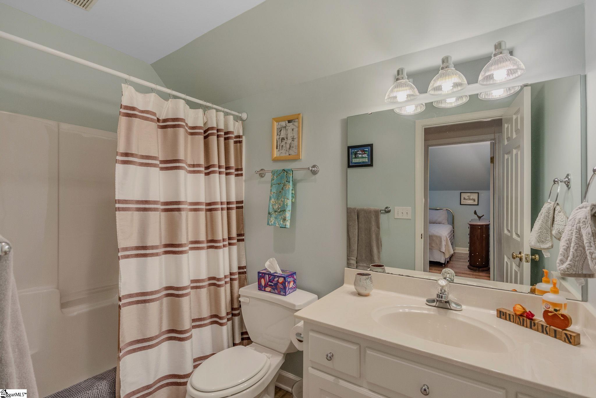 Bathroom with striped shower curtain, bathtub, toilet, and white vanity beneath a large mirror.
