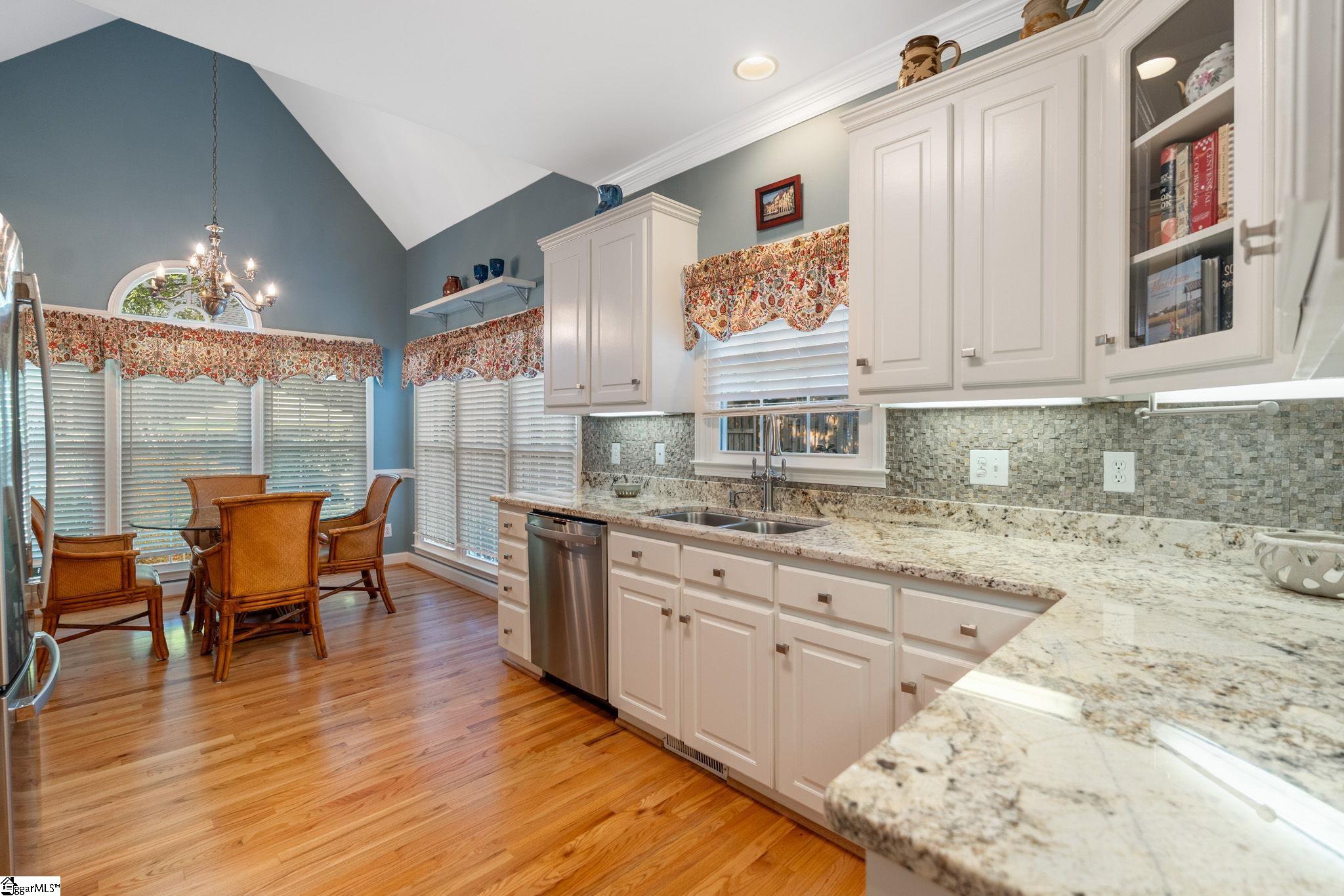 Kitchen with granite counters and white cabinets beside a dining area with a chandelier.