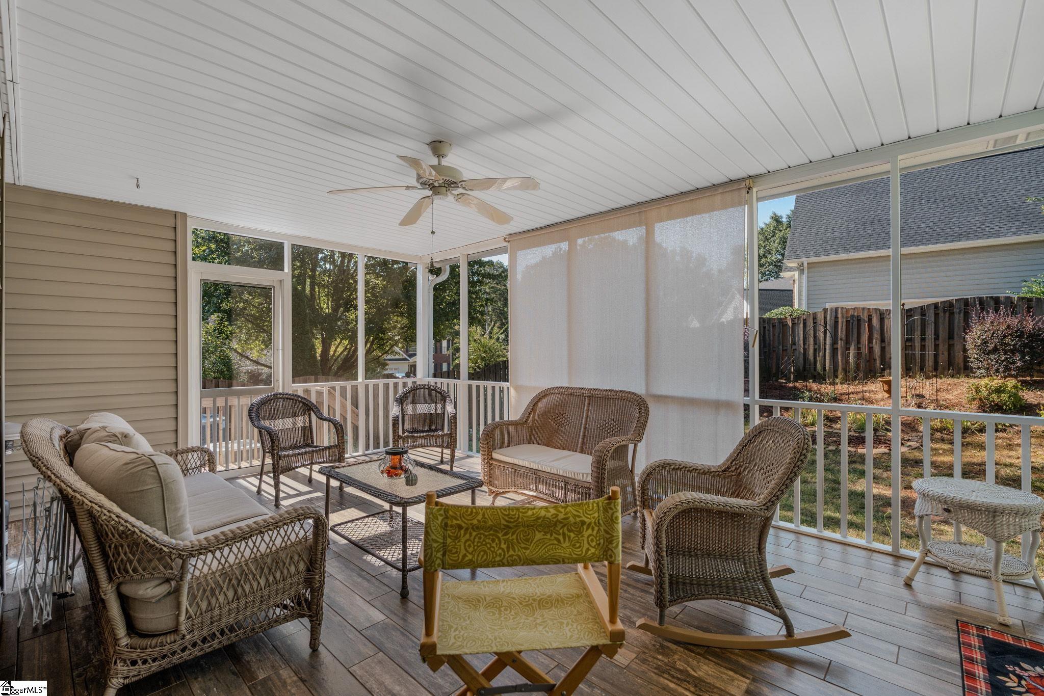 Screened porch with wicker seating, a ceiling fan, and views of the fenced backyard.