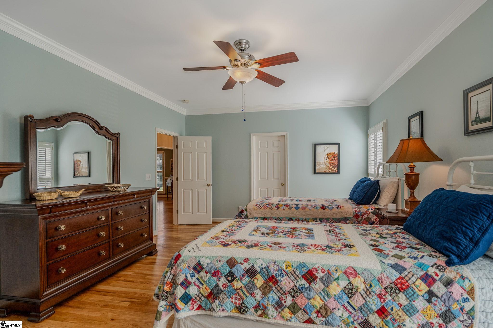 Furnished bedroom with two patchwork-quilt beds, blue pillows, and a dark wood dresser with mirror.