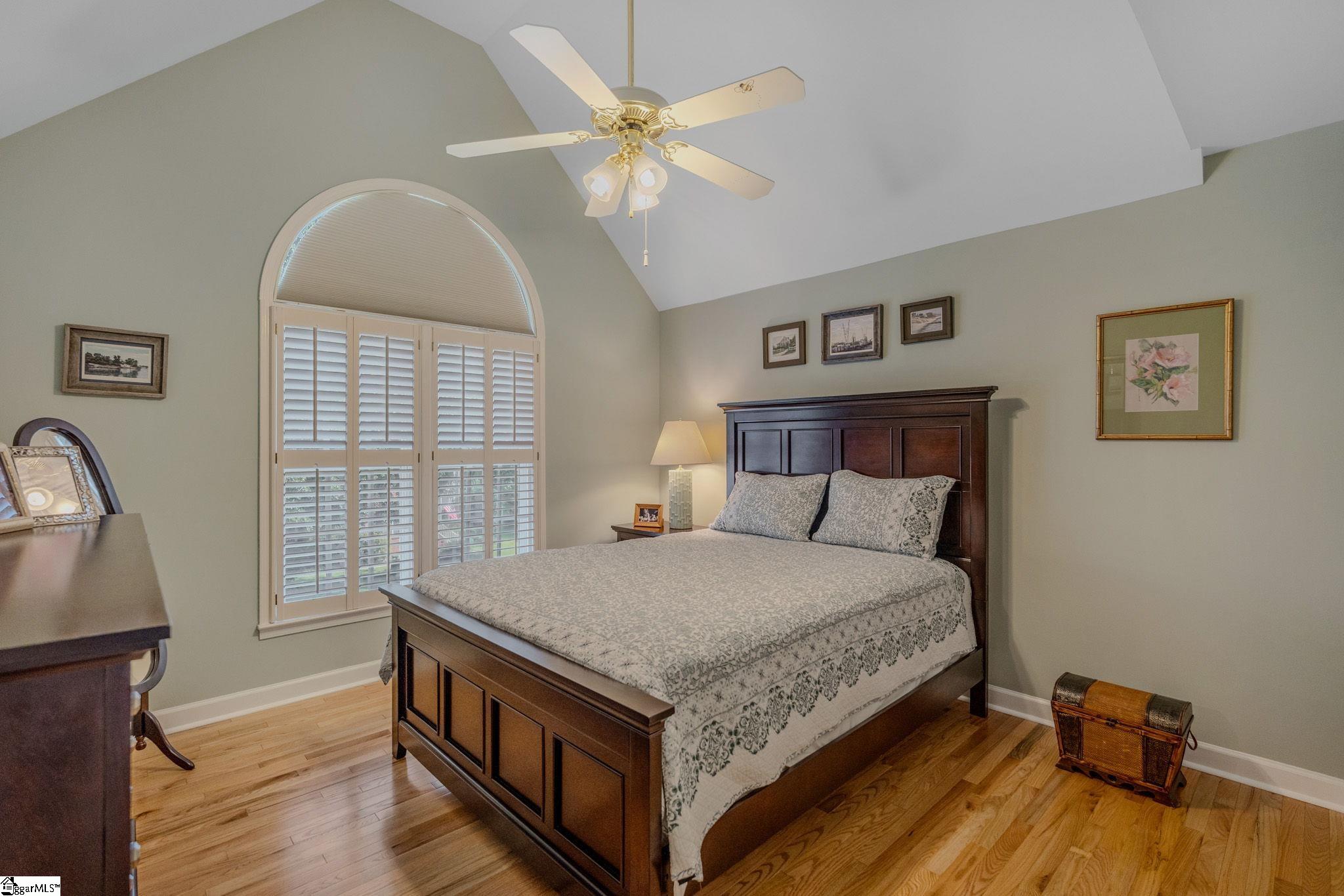 Furnished bedroom with a dark wood bed, hardwood floors, and an arched shuttered window.