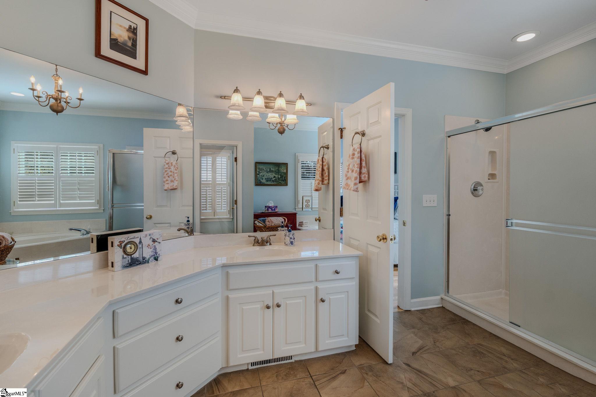 Bathroom with a long white vanity, mirrored wall, pale blue walls, and glass-enclosed shower.