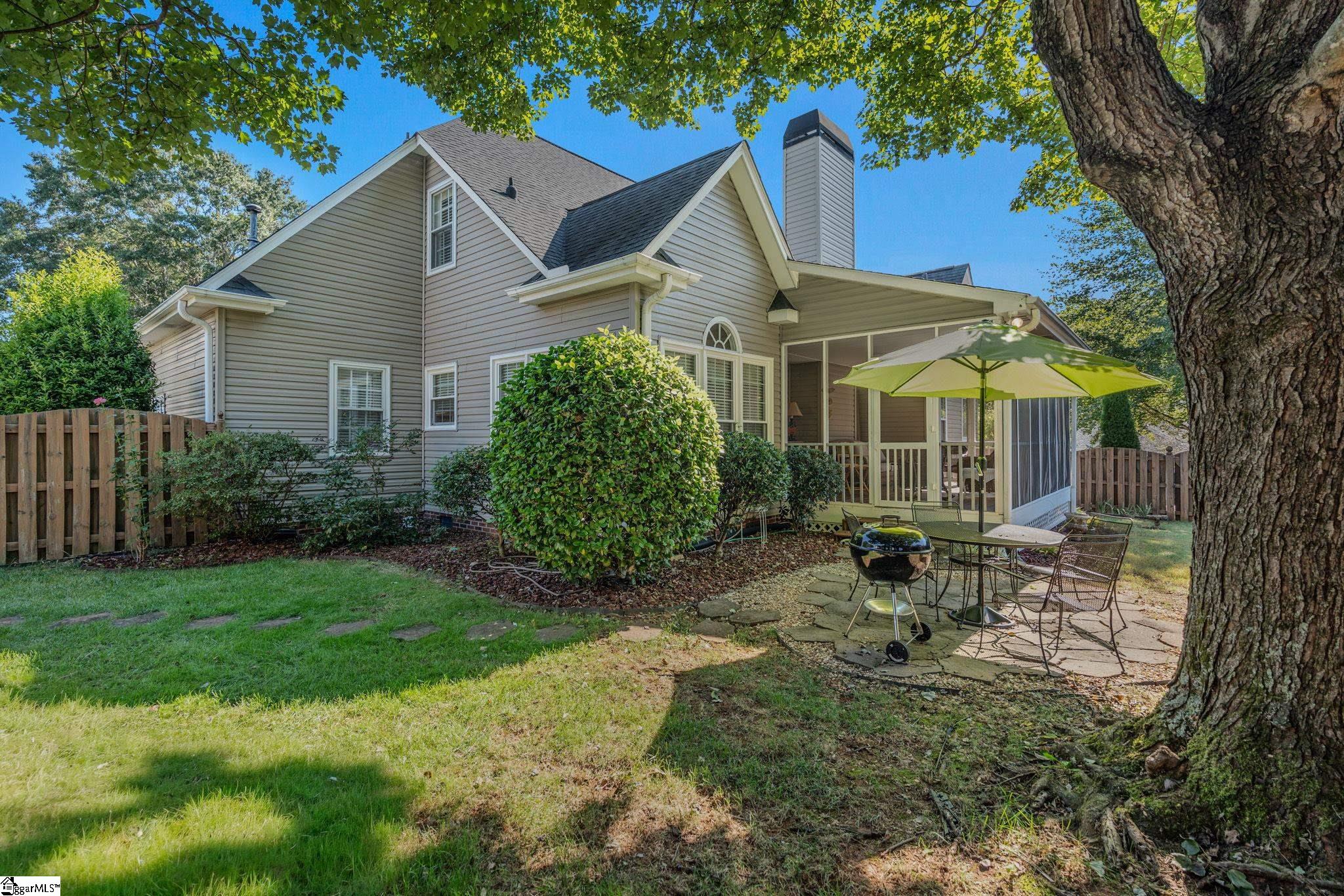 Home’s rear exterior with a screened porch and patio beneath a large shade tree.