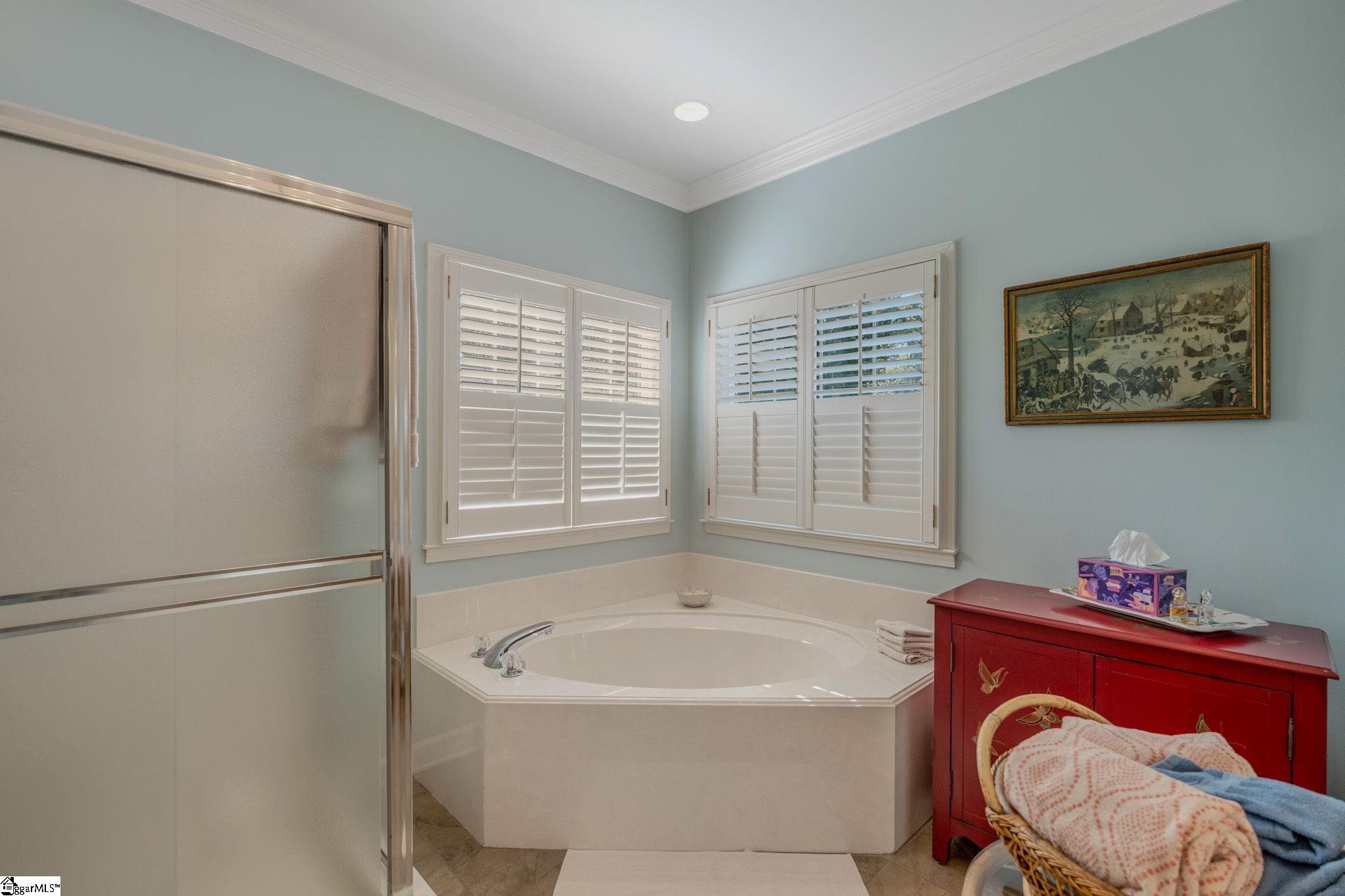 Bathroom with a corner soaking tub, glass shower enclosure, and shuttered windows.