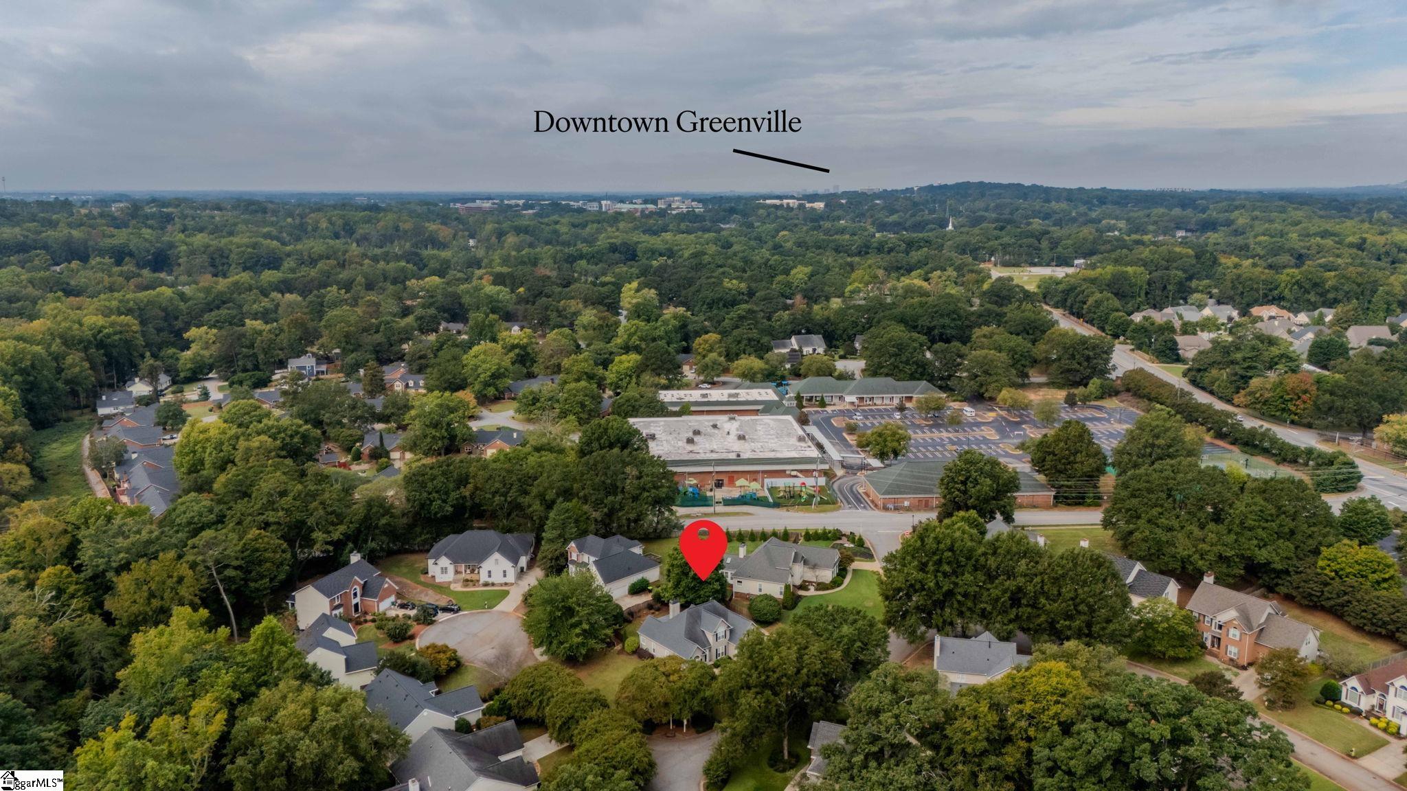 Aerial view of a tree-lined neighborhood with a home marker and distant downtown Greenville.