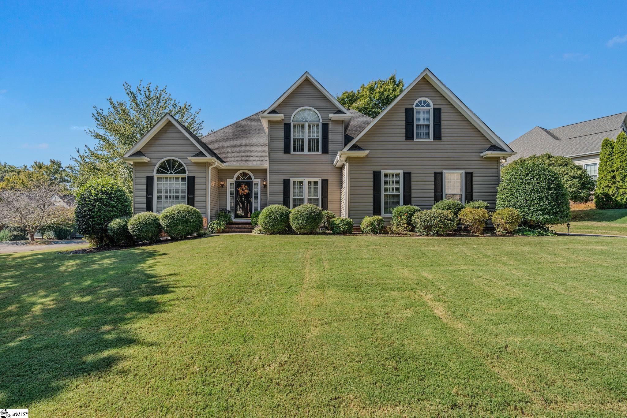 Two-story taupe house with arched windows, black shutters, and a broad front lawn.