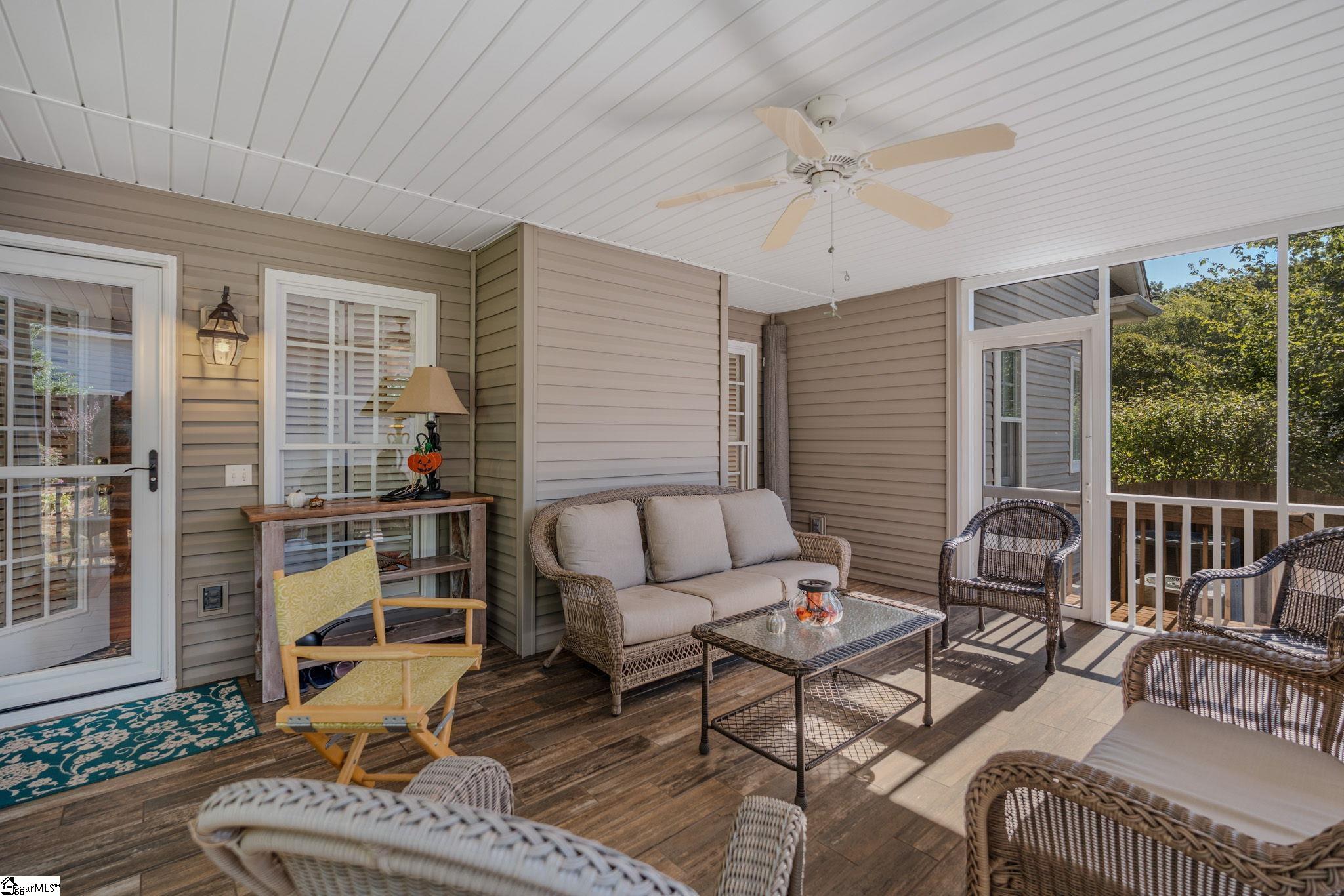 Furnished covered porch with wicker seating, screened walls, and a ceiling fan.