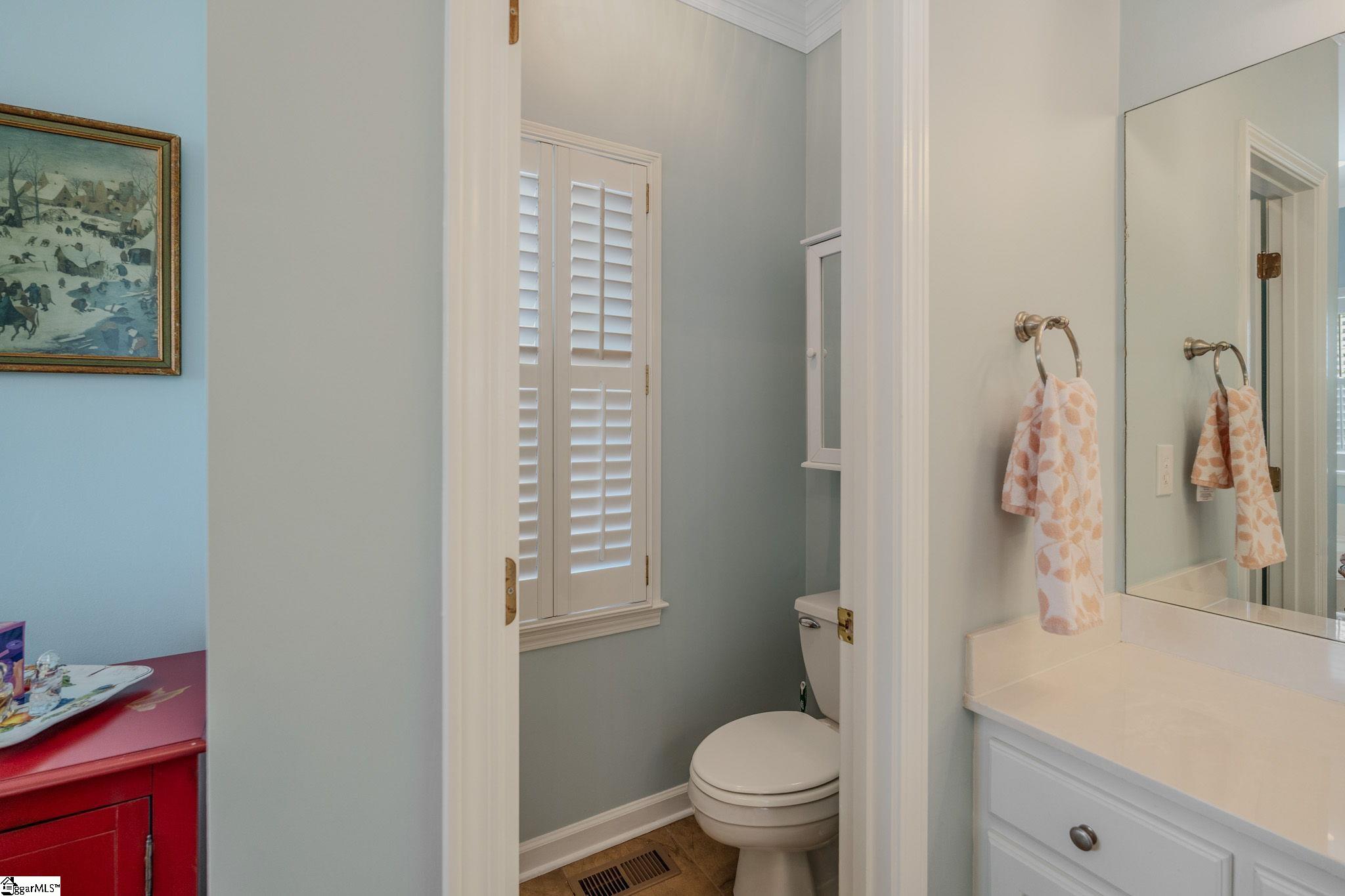 Bathroom with shuttered window, toilet, white vanity, large mirror, and patterned towels.