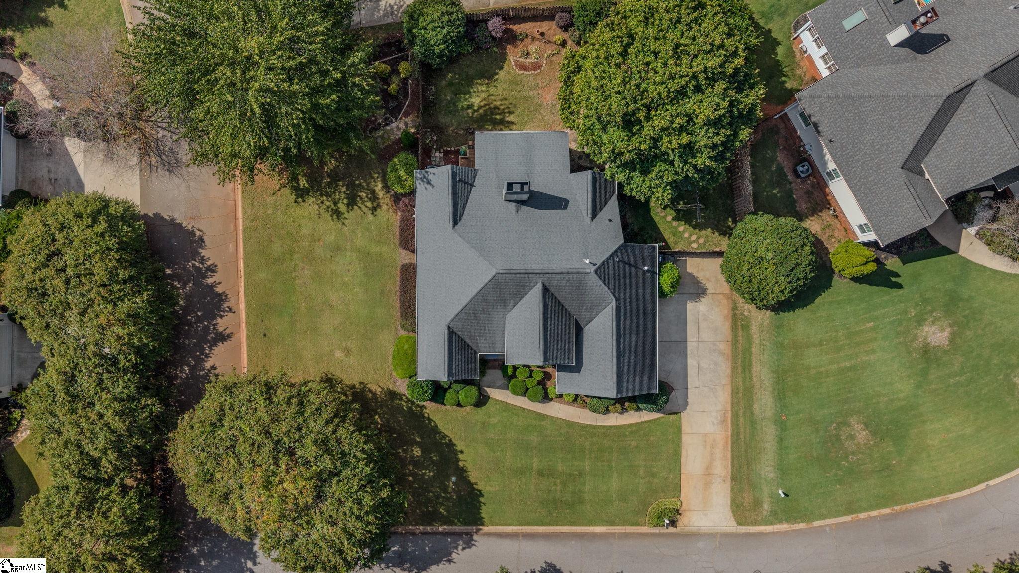 Aerial view of a home with a broad lawn, concrete driveway, and mature trees.