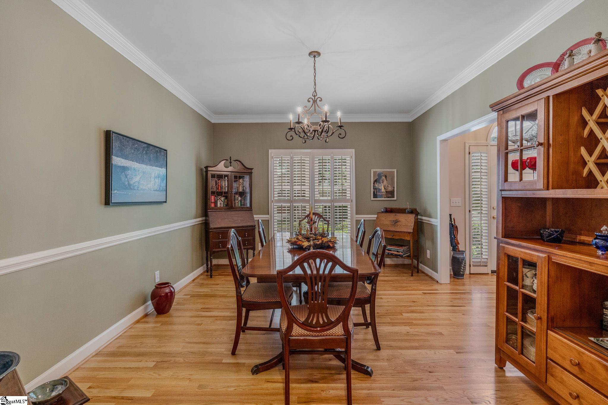 Furnished dining room with a wood table, hardwood floors, chandelier, and plantation shutters.