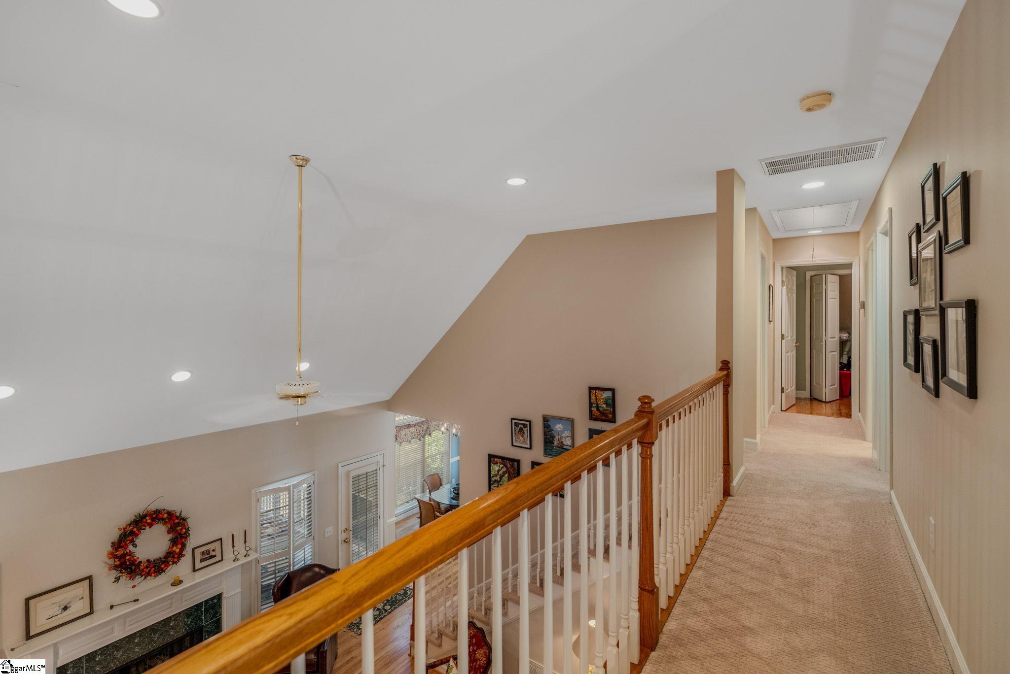 Upstairs hallway and landing with a wood railing overlooking a living room and fireplace.