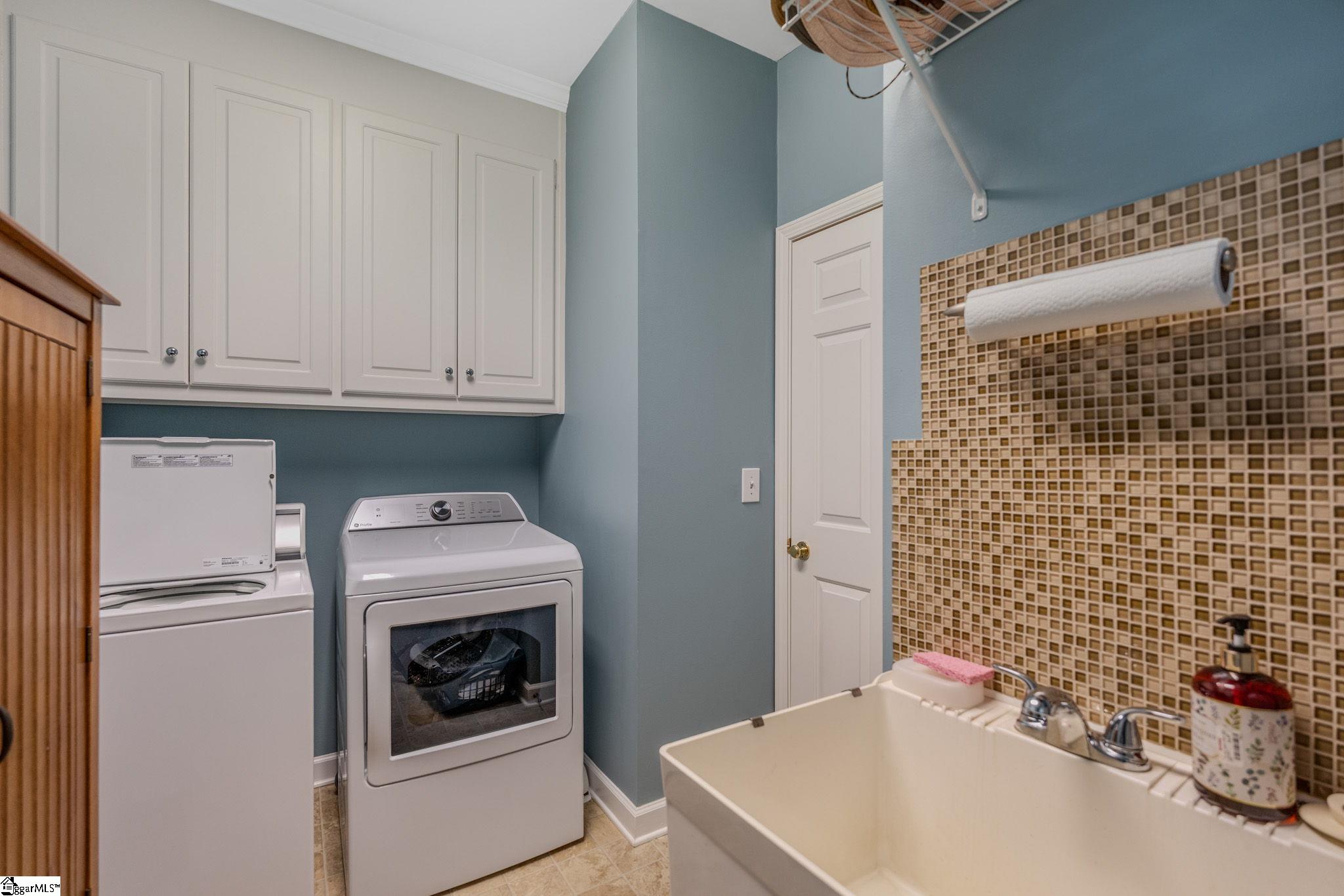Laundry room with washer and dryer, white cabinets, and a utility sink with mosaic tile backsplash.
