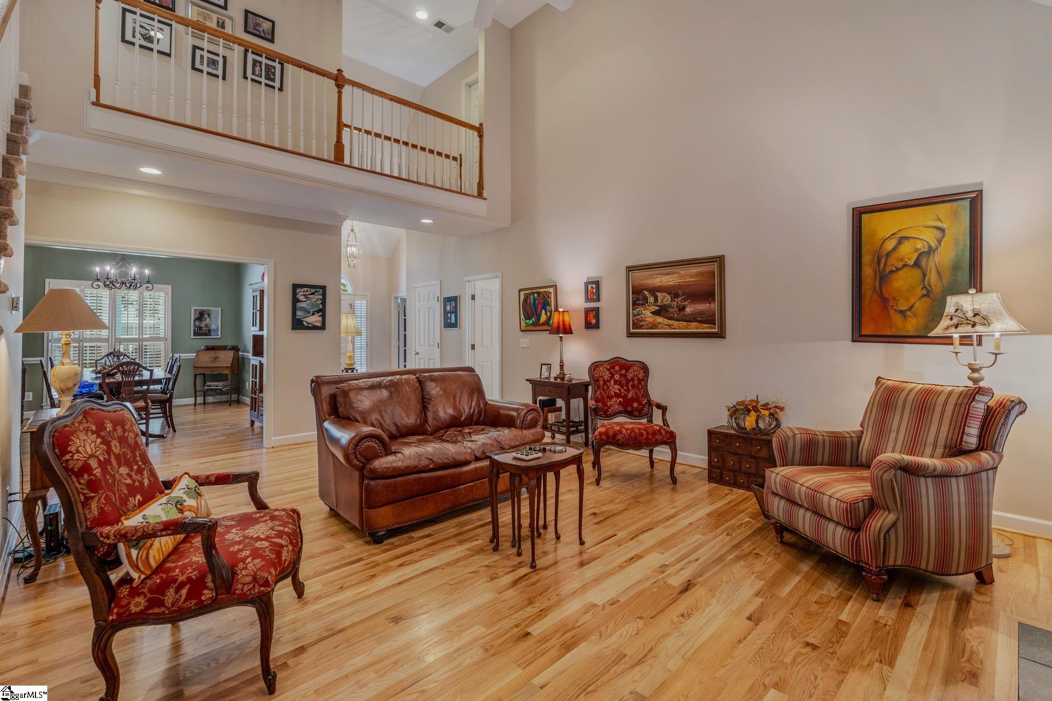 Furnished living room with hardwood floors, a leather sofa, and an upstairs gallery overlooking the adjoining dining area.