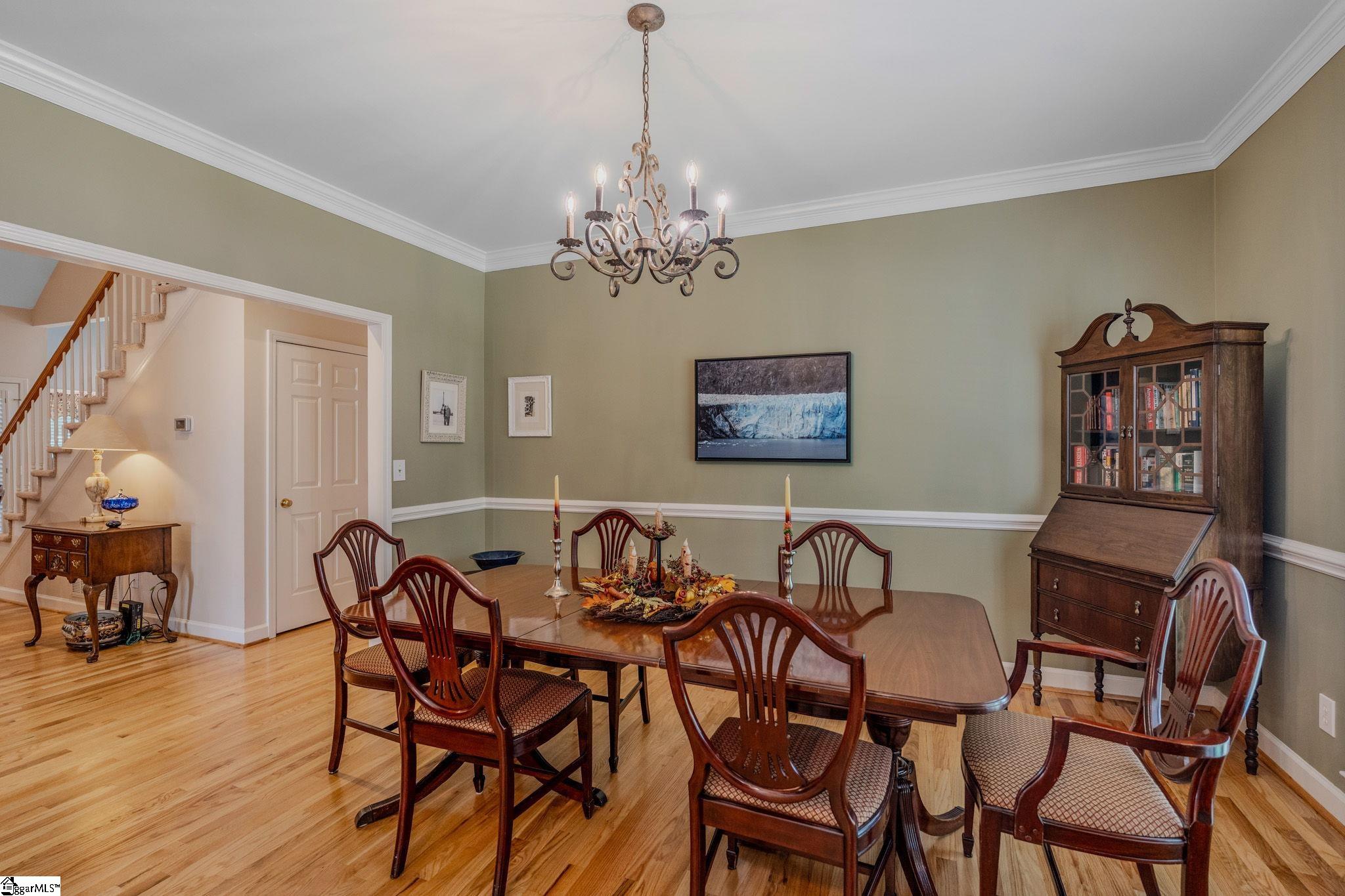 Furnished dining room with a wooden table, chandelier, hardwood floors, and staircase