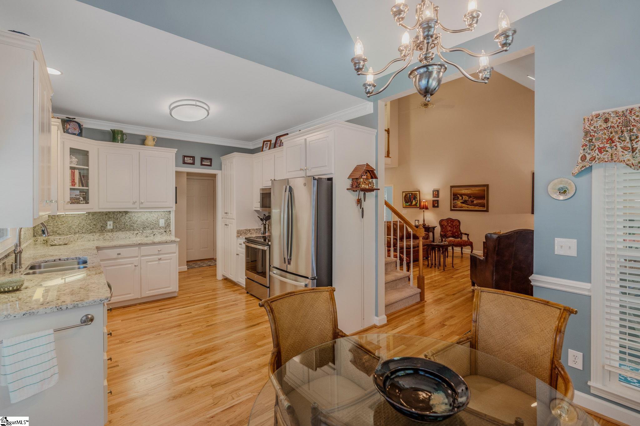 Kitchen and dining area with white cabinets, stainless steel appliances, granite counters, and hardwood floors.