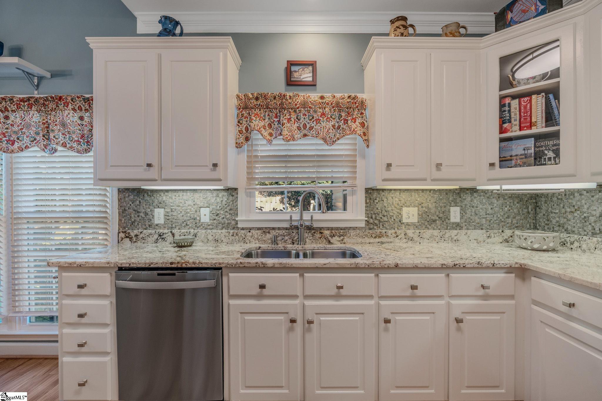 Kitchen with white cabinets, granite counters, mosaic backsplash, and a sink beneath a floral-valance window.