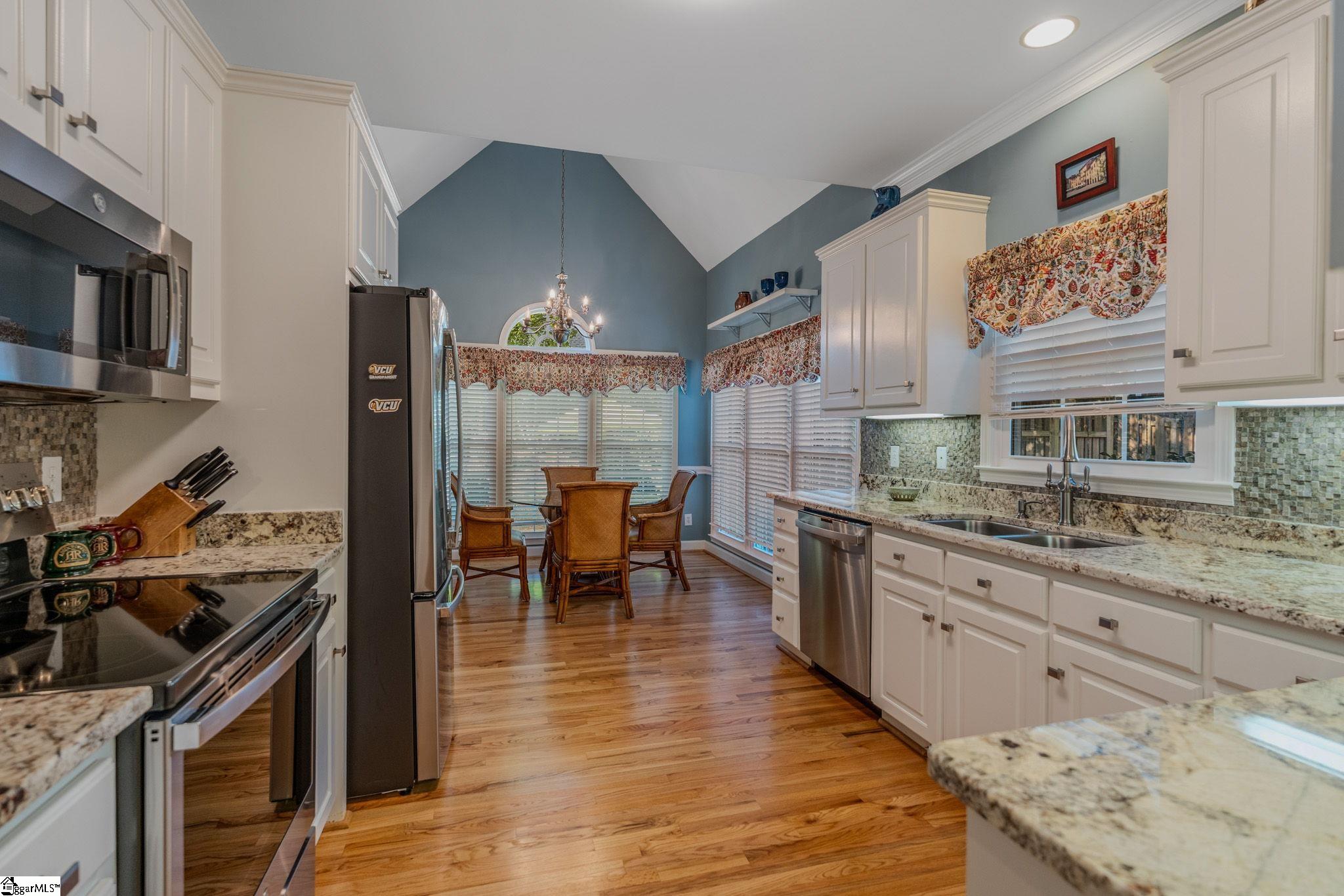 Kitchen with white cabinets, granite counters, stainless steel appliances, and a dining table beneath a vaulted blue ceiling.