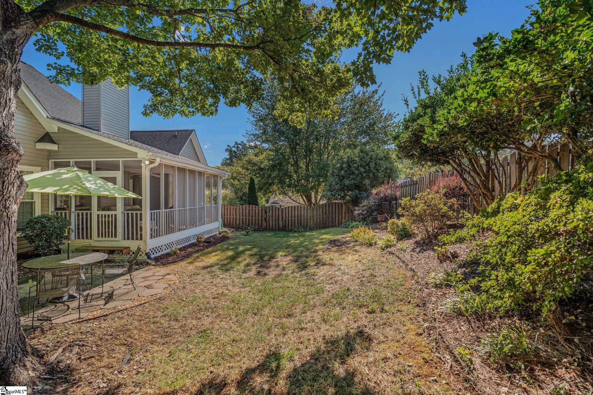 Backyard with a screened porch, shaded patio seating, mature trees, and a wooden privacy fence.
