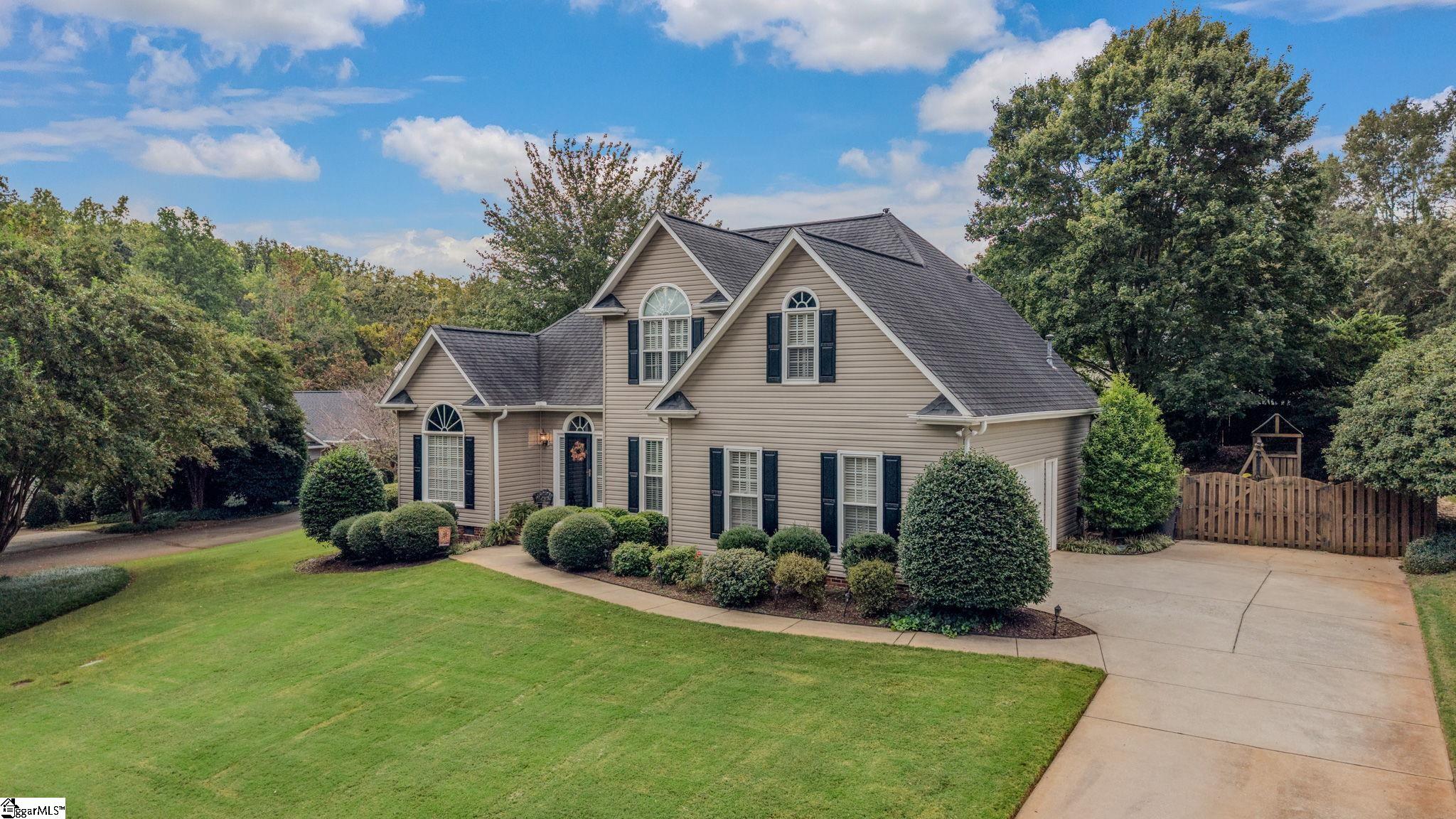 Beige two-story home with gabled roof, landscaped lawn, broad driveway, and wooden fence.