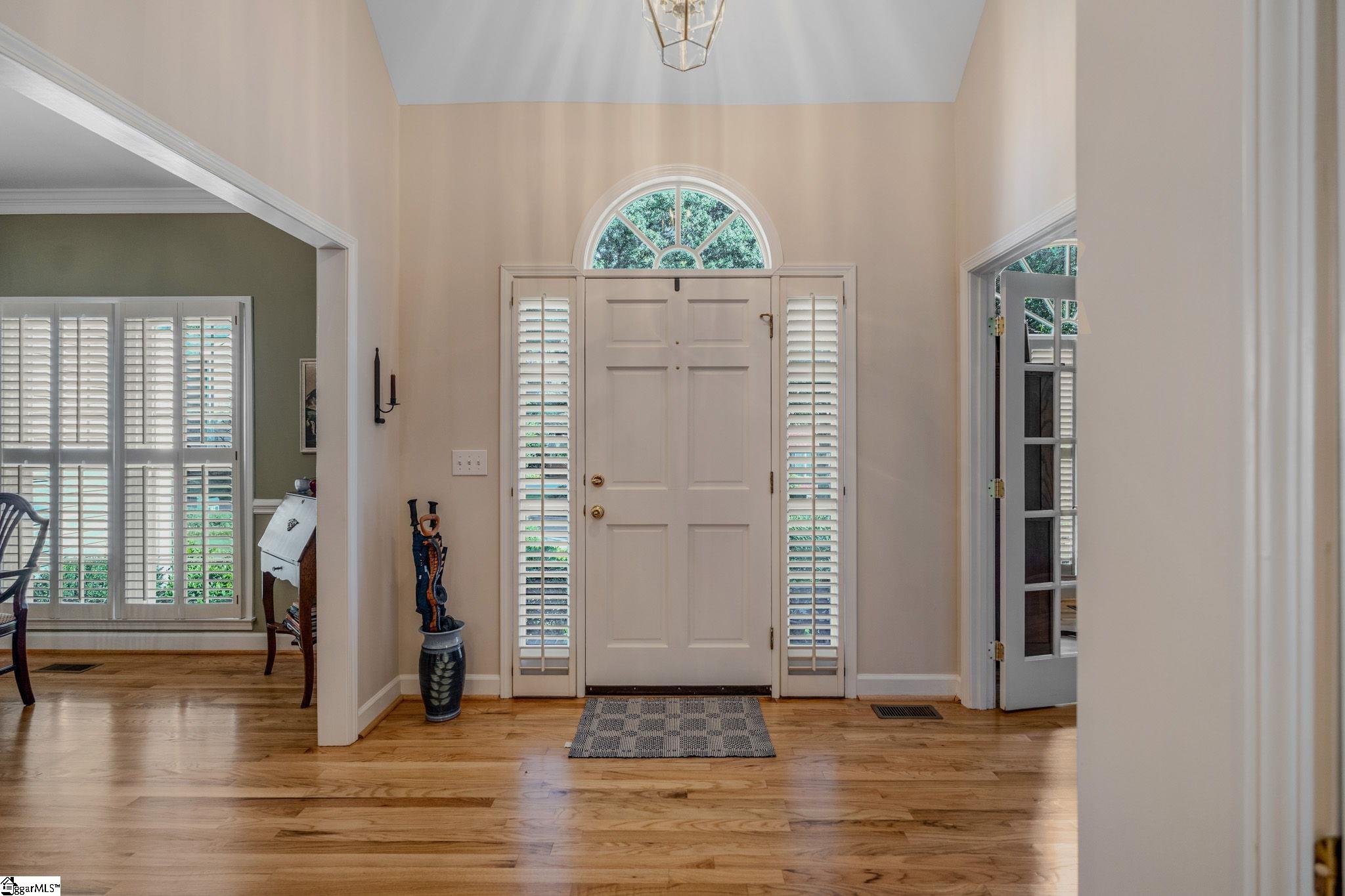 Entry foyer with a paneled front door, arched fanlight, shuttered sidelights, and hardwood floors.