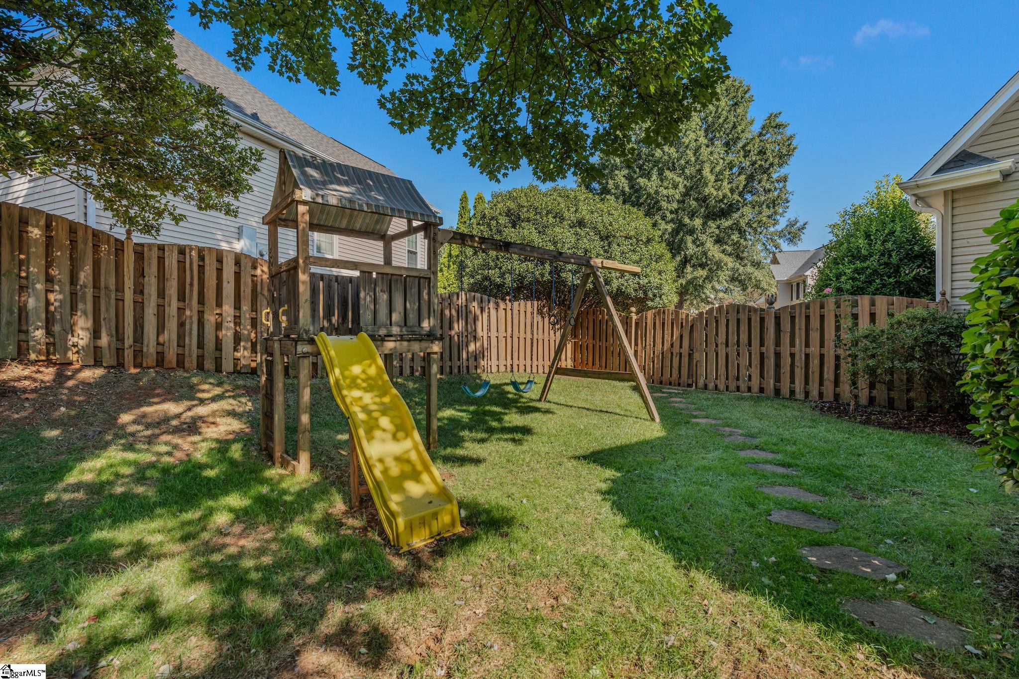 Fenced backyard with a wooden playset, yellow slide, and swings.