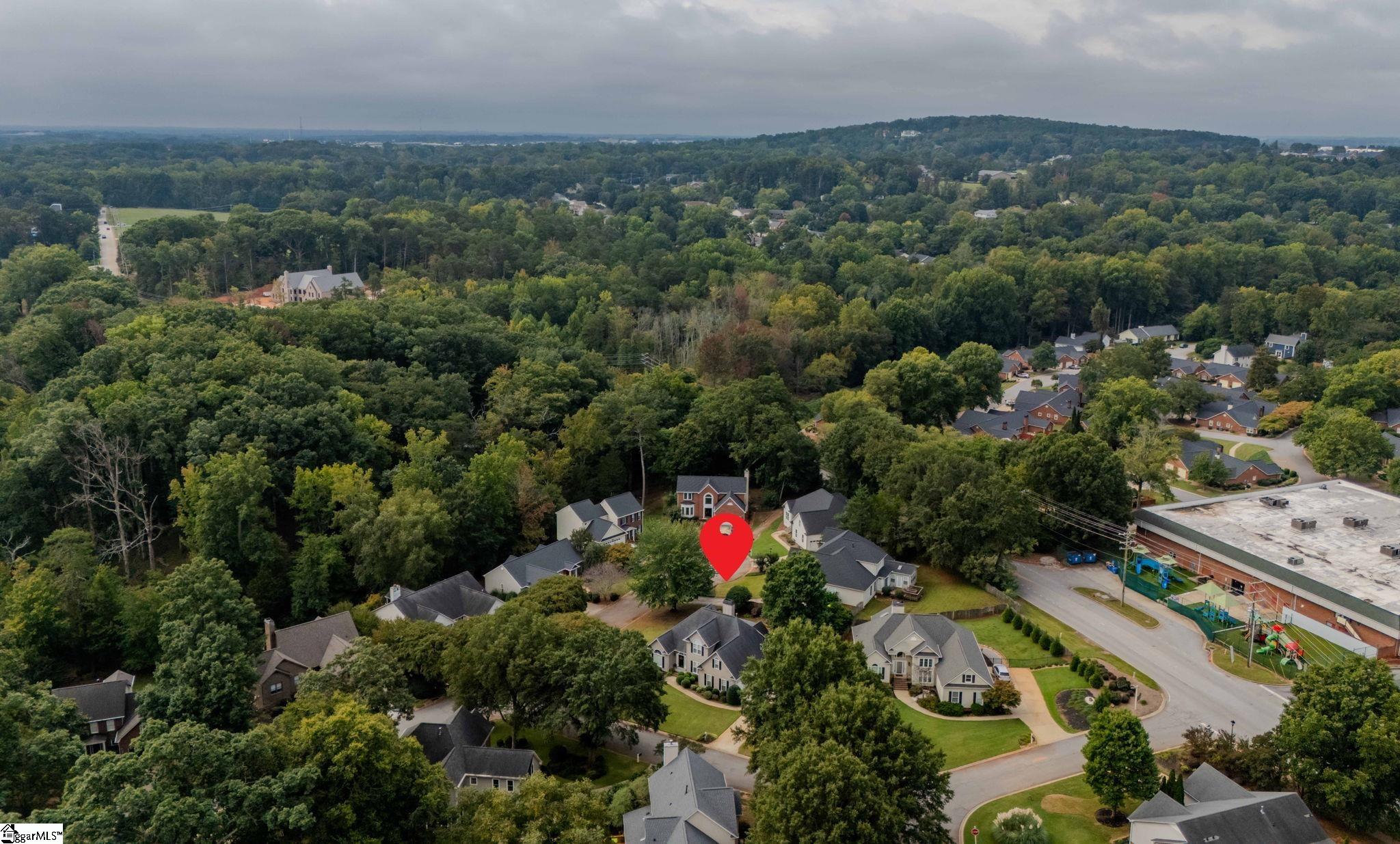 Aerial neighborhood view with a red map pin marking a home among trees and nearby houses.