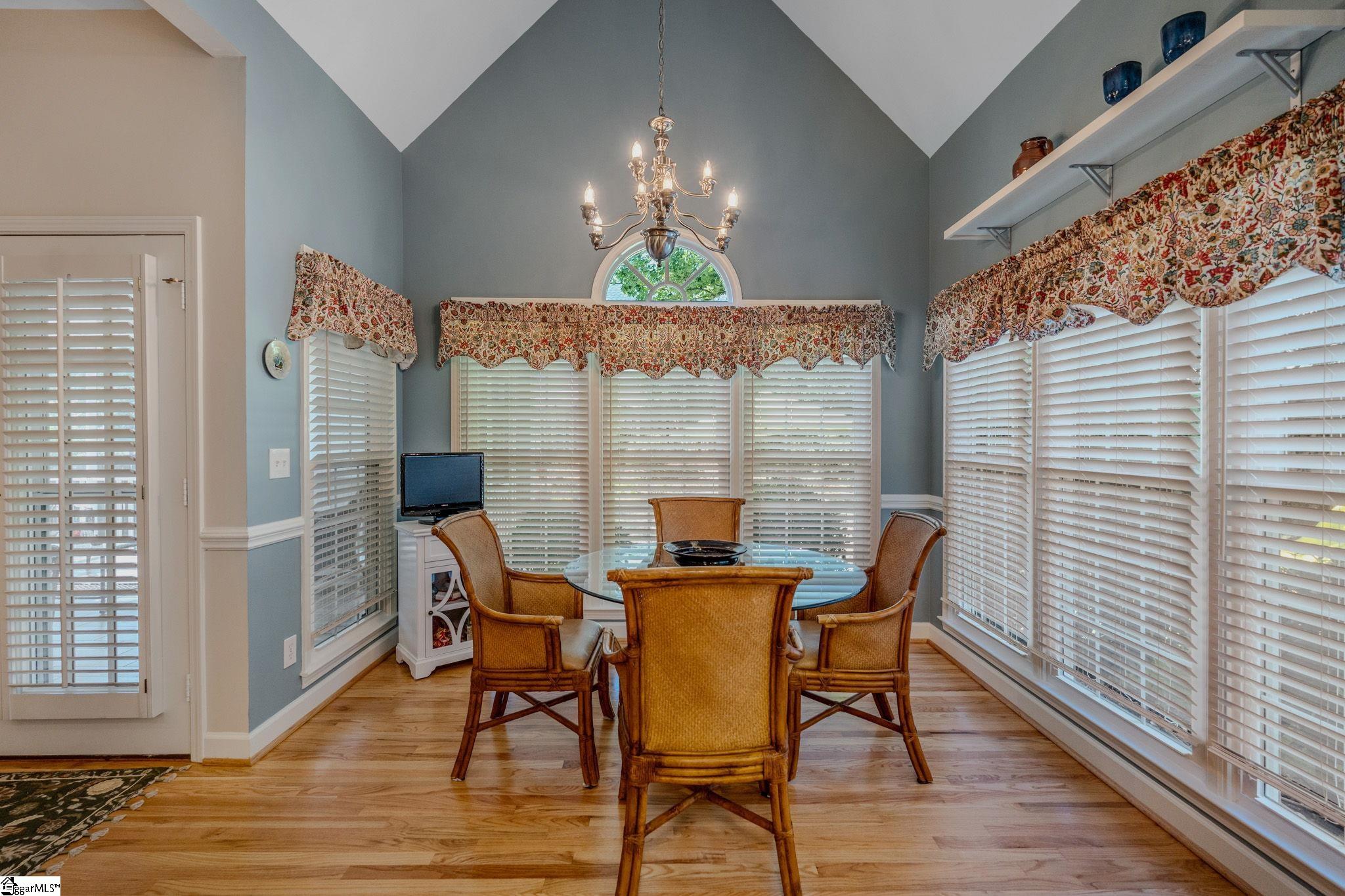 Dining room with a glass-top table, wicker chairs, vaulted ceiling, and shuttered windows.