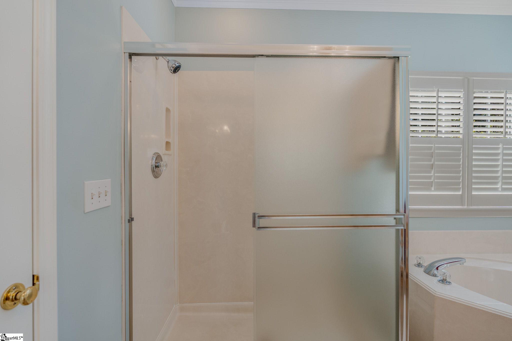 Bathroom with a glass-enclosed shower, built-in tub, and plantation shutters.