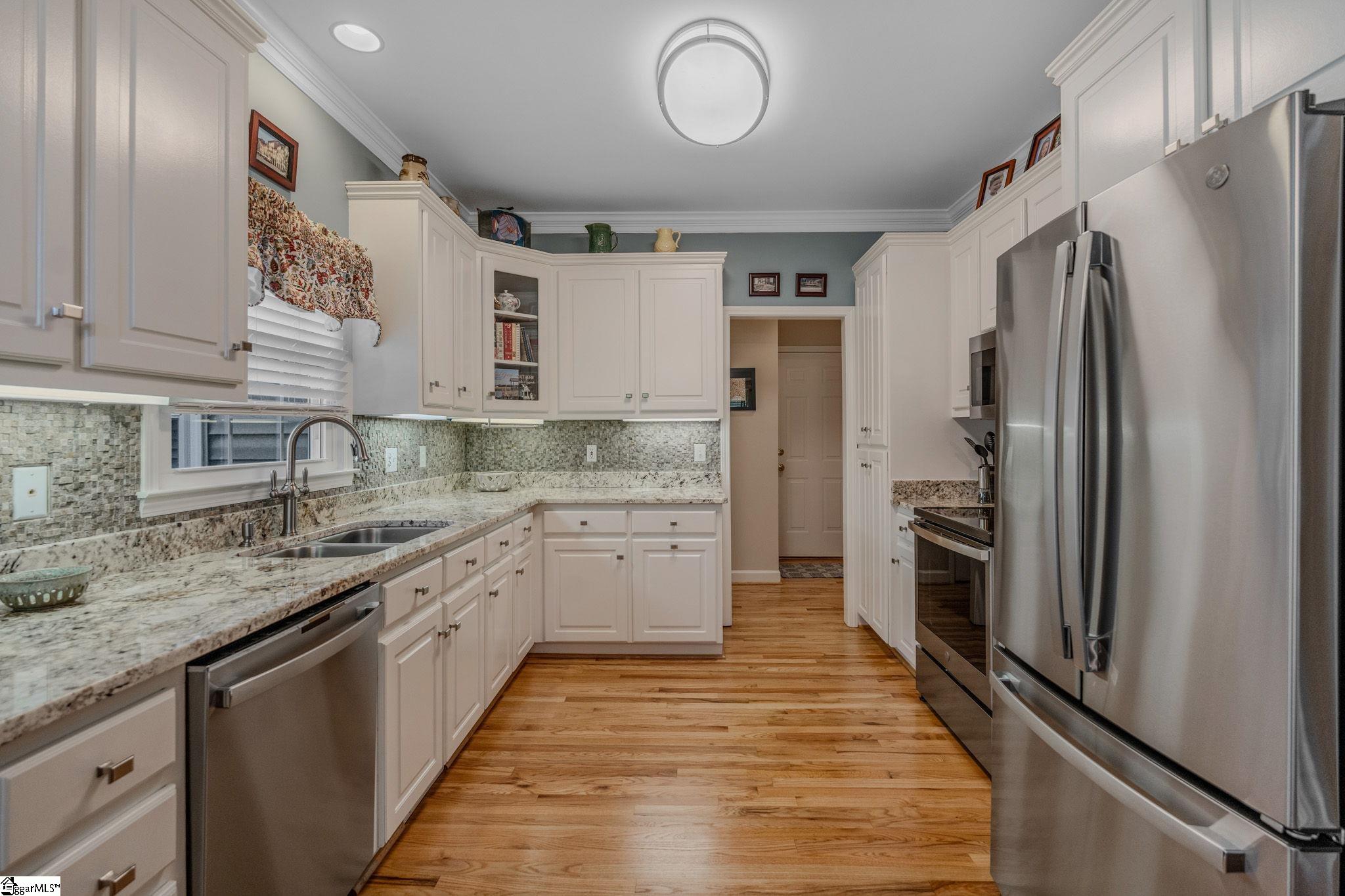 Kitchen with white cabinets, granite counters, stainless steel appliances, and warm hardwood floors.