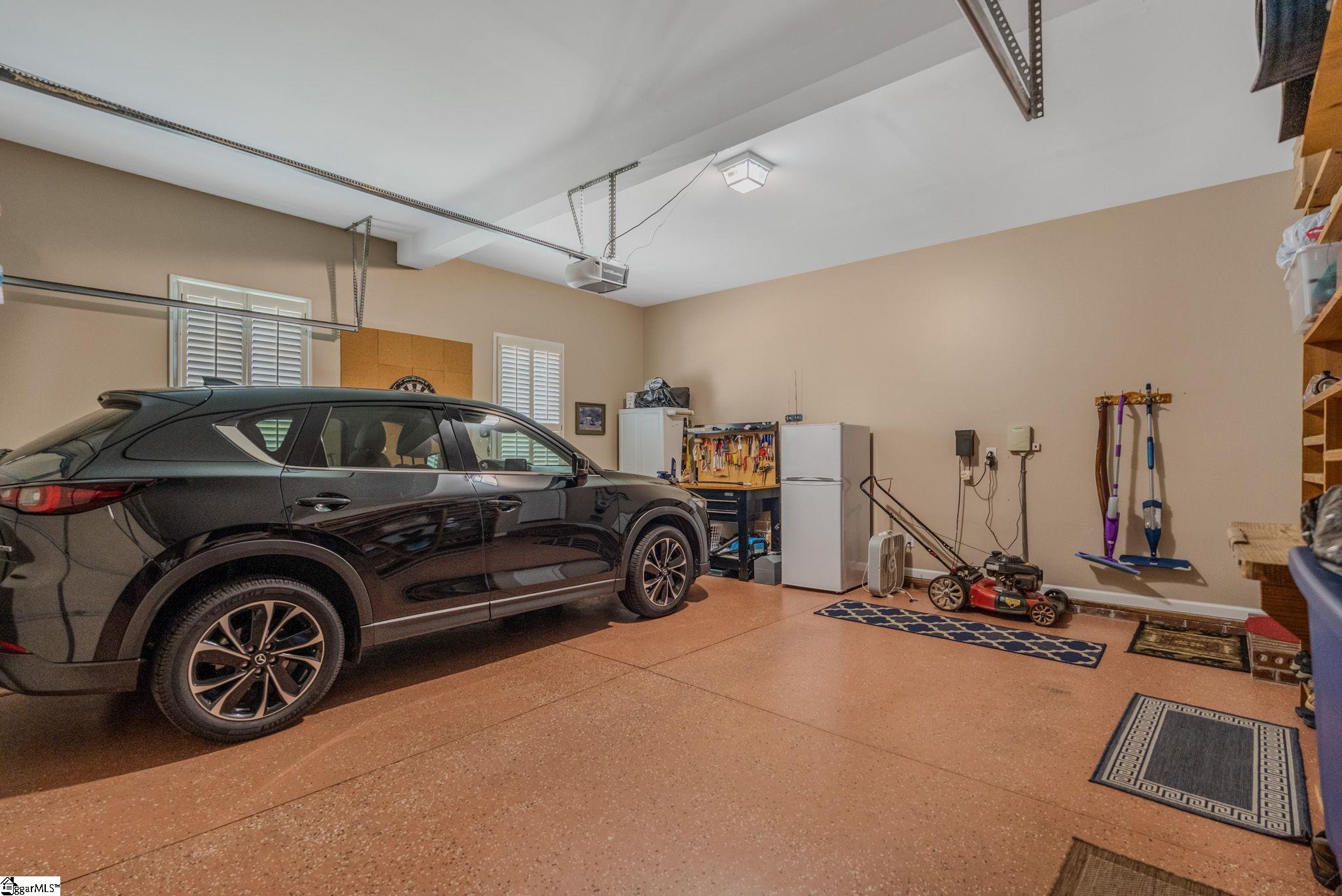 Garage with a black SUV, tool bench, refrigerators, and lawn equipment.