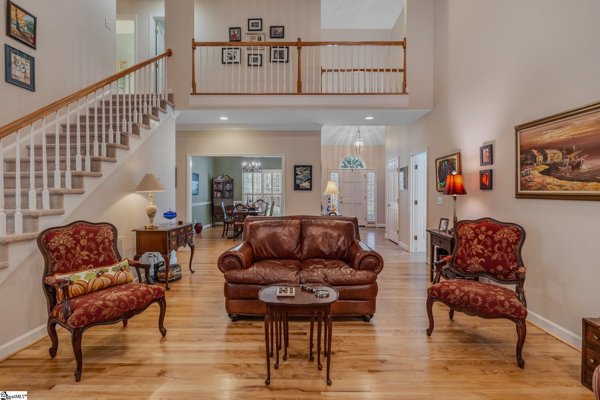 Furnished living room with a leather sofa, patterned armchairs, hardwood floors, and a carpeted staircase.