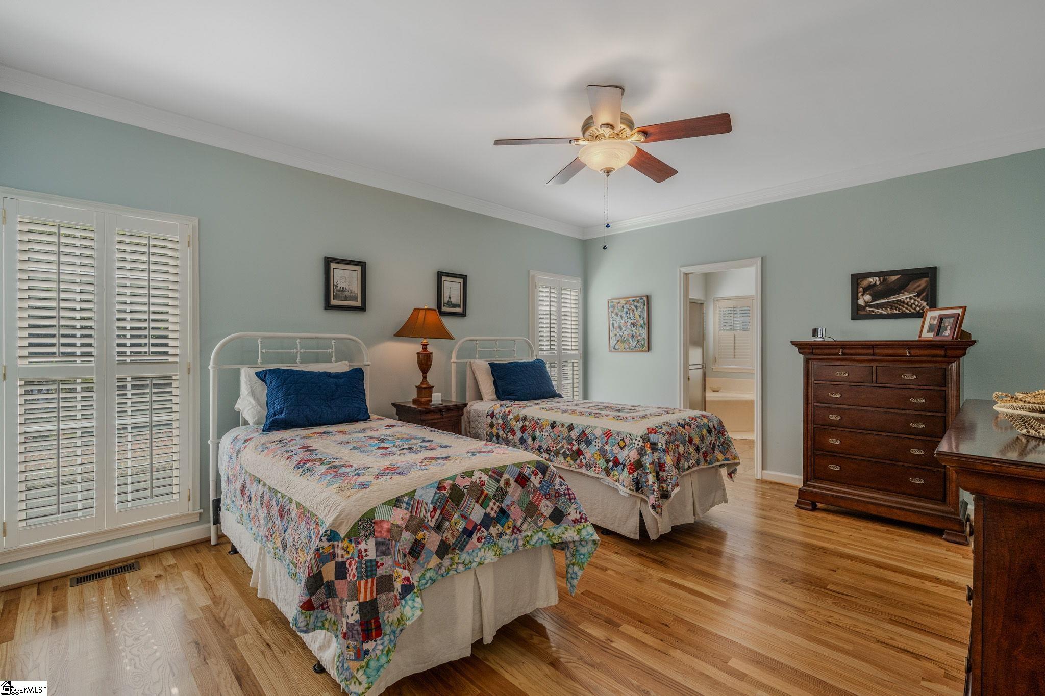 Bedroom with twin beds, colorful patchwork quilts, plantation shutters, and hardwood floors.