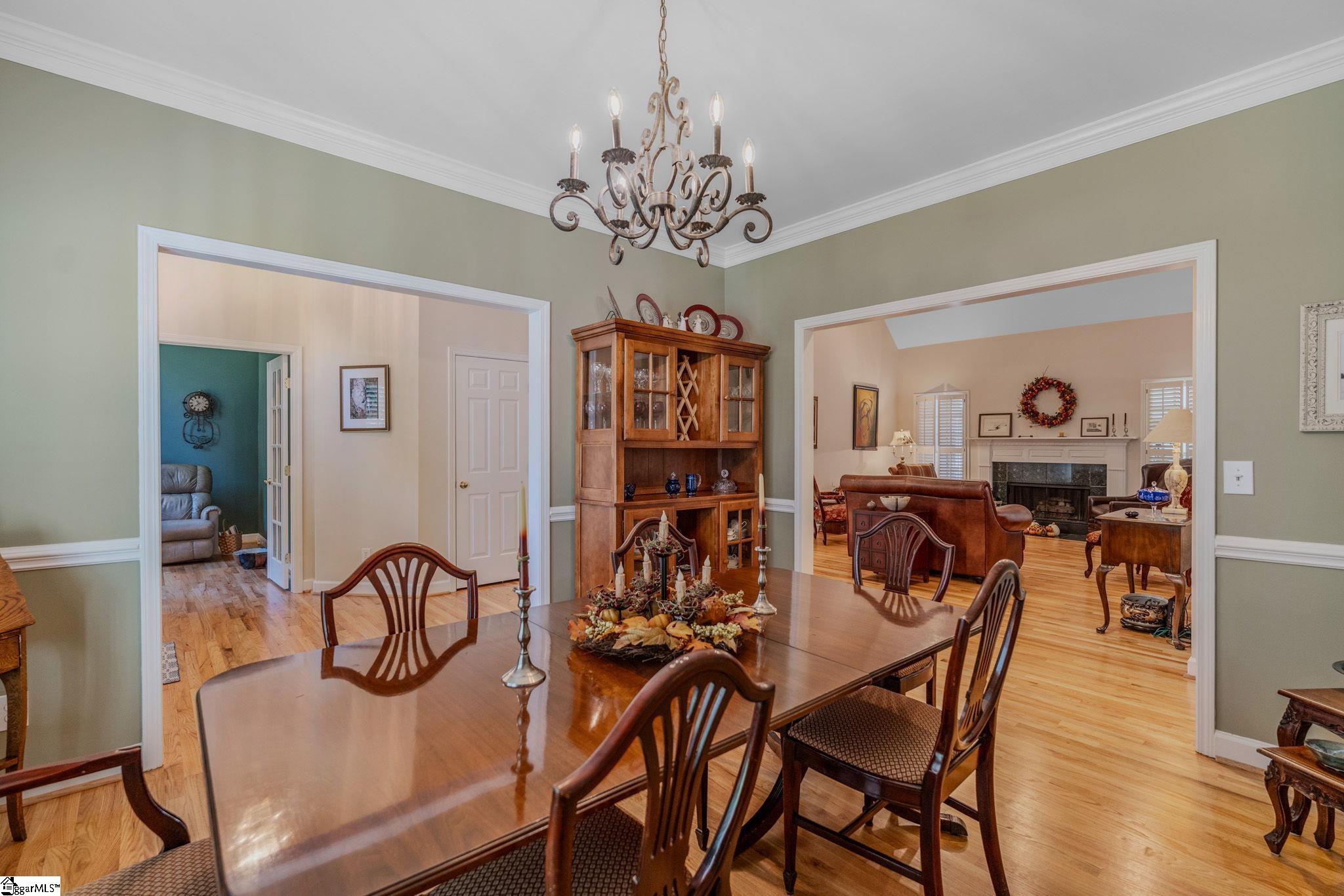 Furnished dining room with a polished wood table, chandelier, and wide openings to adjoining rooms.