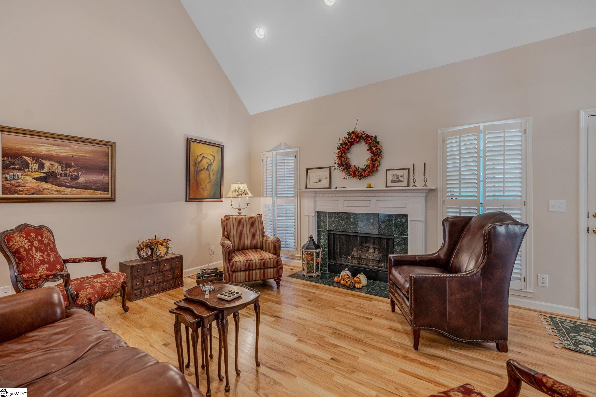 Furnished living room with a dark stone fireplace, hardwood floors, and shuttered windows.