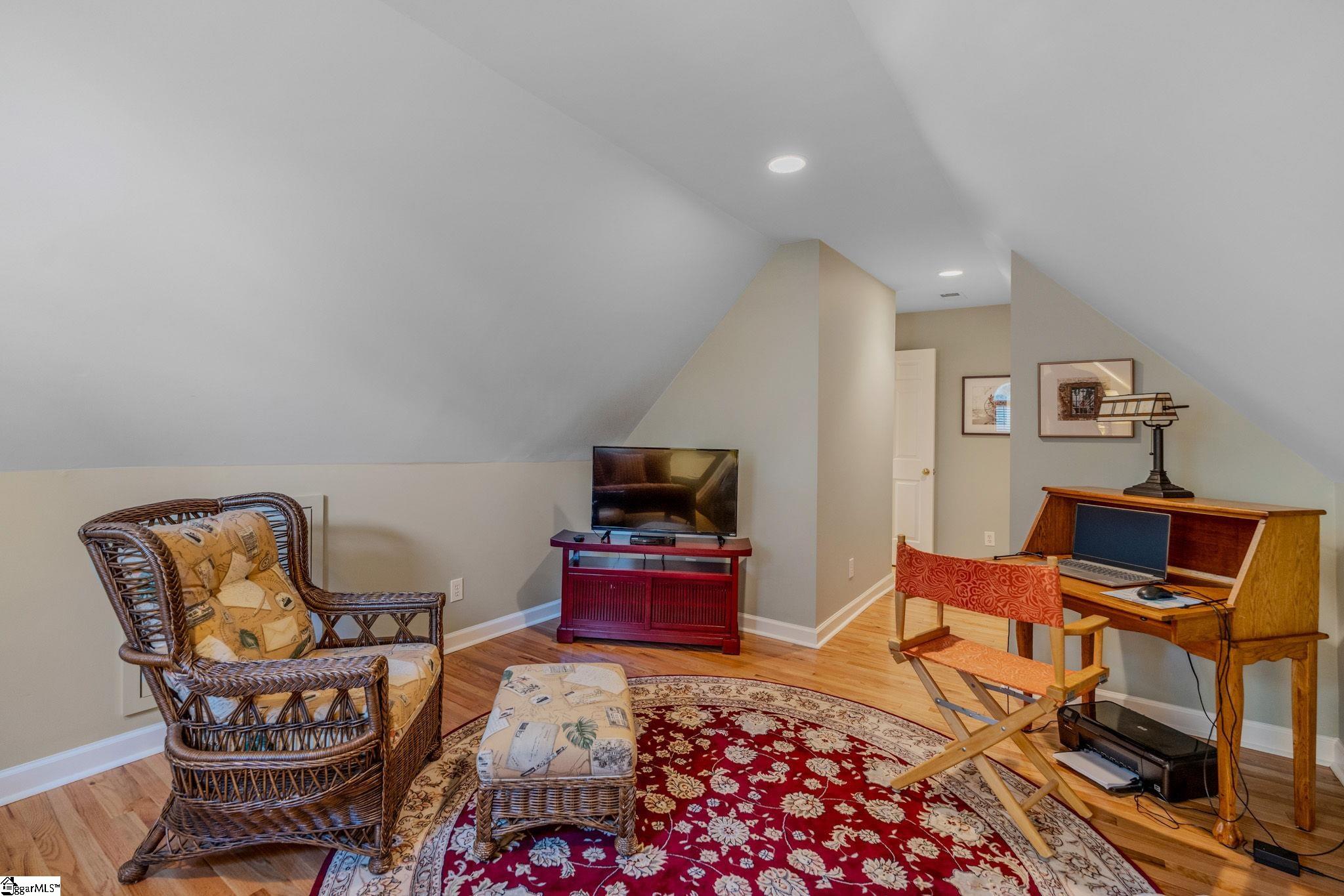 Attic office with a wooden desk, wicker chair, and patterned red rug.