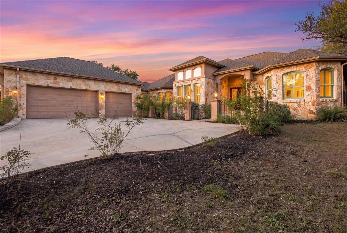 Stone-front home with a three-car garage and wide driveway beneath a pink sunset sky.