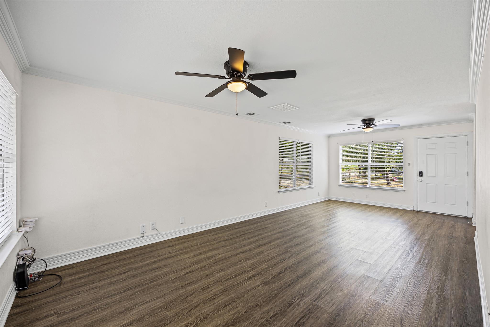 Vacant living room with wood-look floors, two ceiling fans, and windows beside the front door.