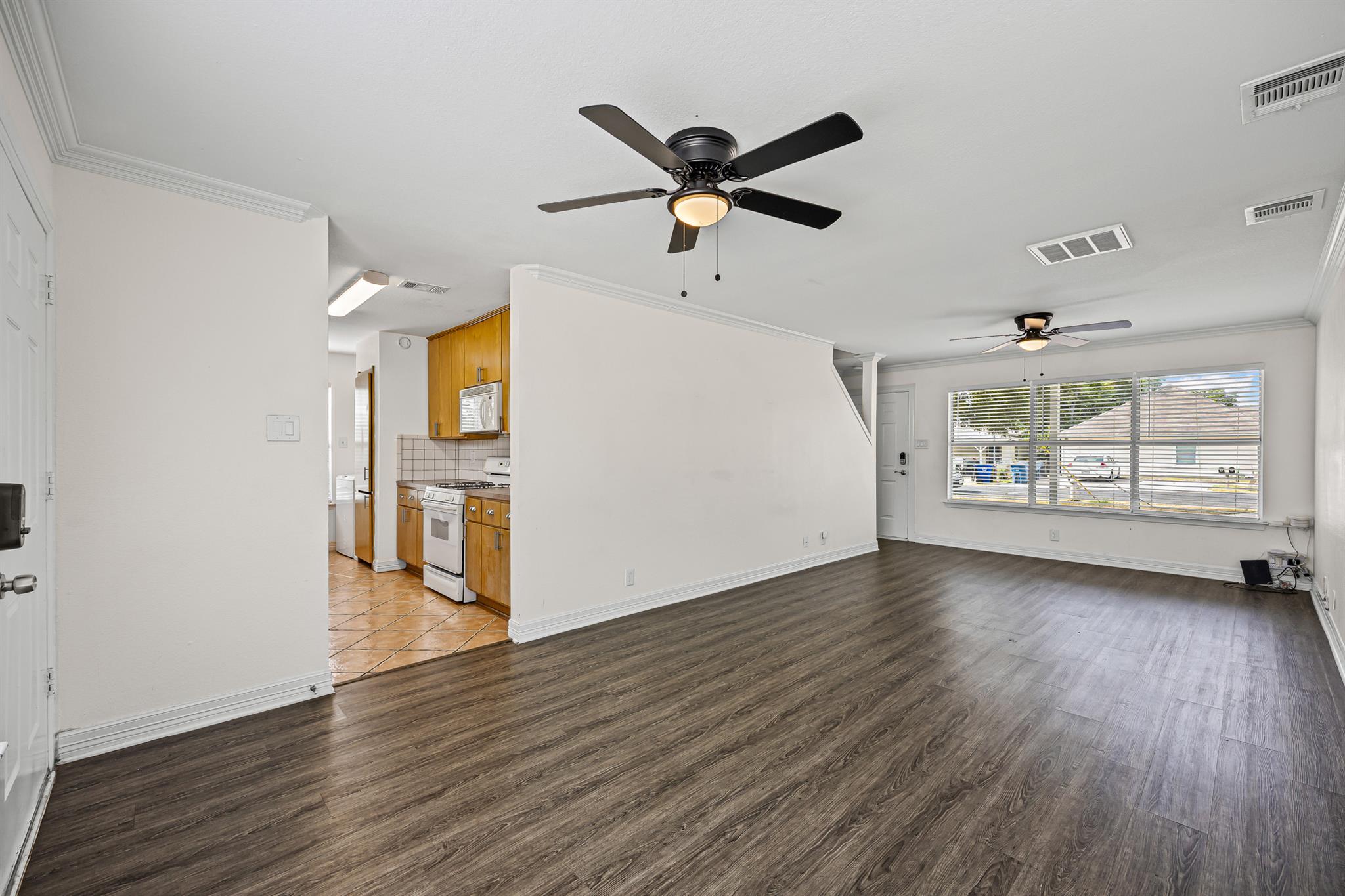 Vacant living room with dark wood-look floors, ceiling fans, and a view into the kitchen.