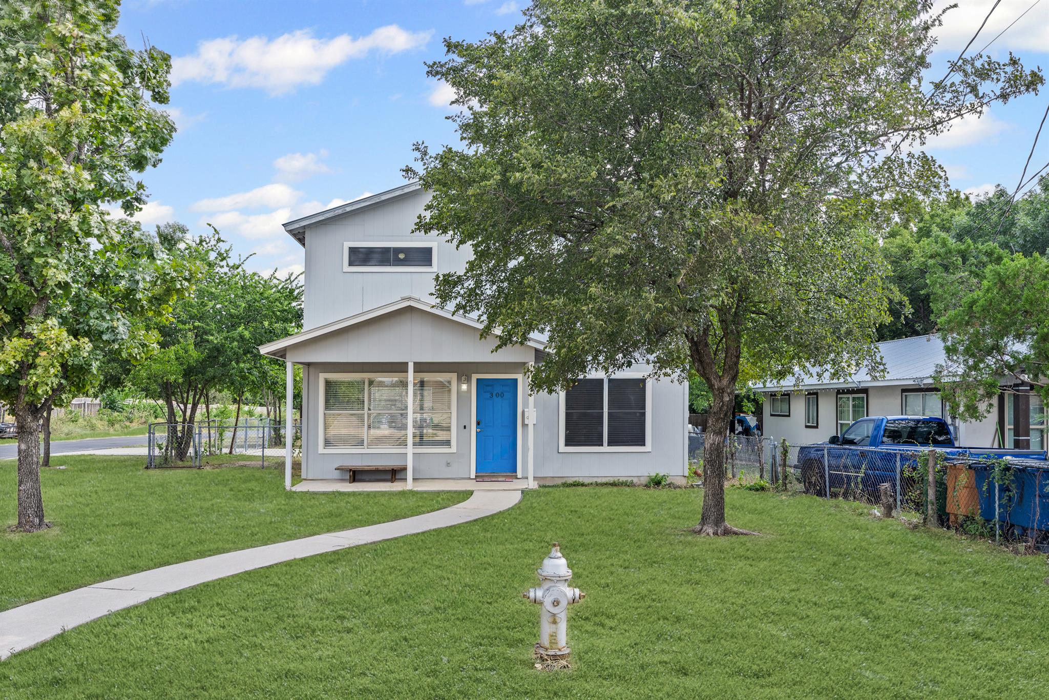 Light-gray two-story home with a bright blue front door, covered porch, and mature trees.
