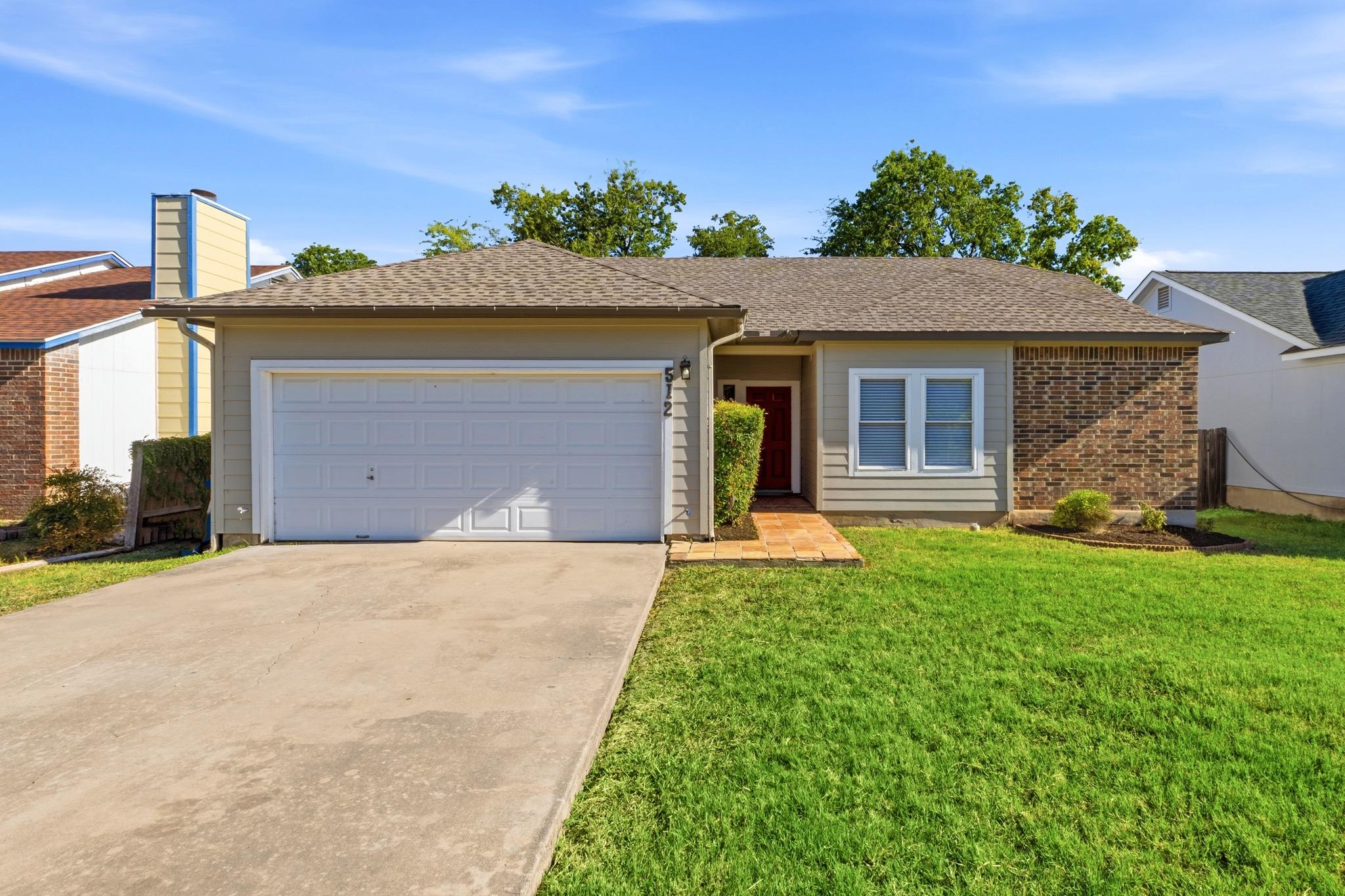 Single-story home with a two-car garage, red front door, brick accents, and a green lawn.