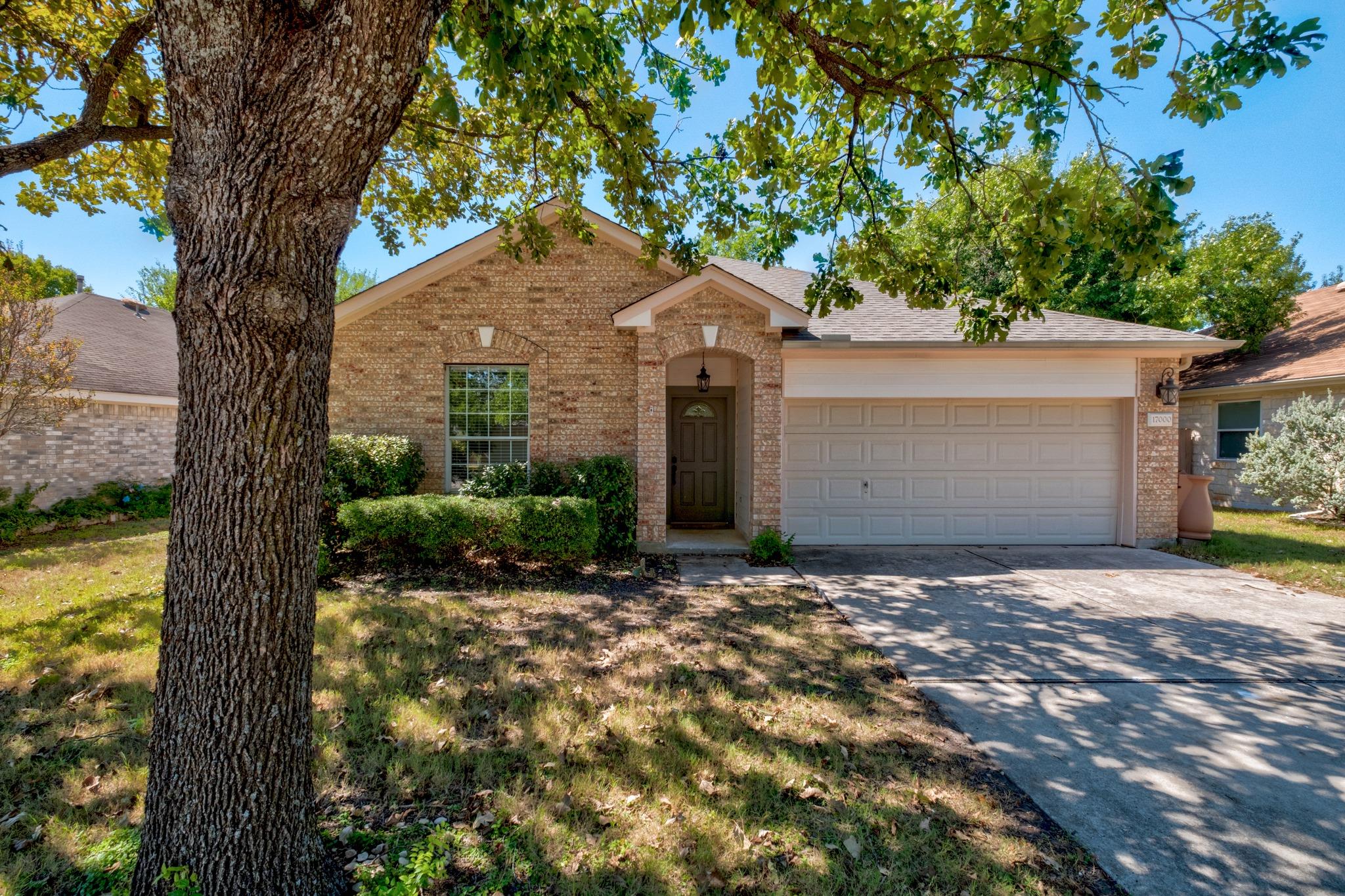 Brick single-story home with a two-car garage, shaded by a large tree.