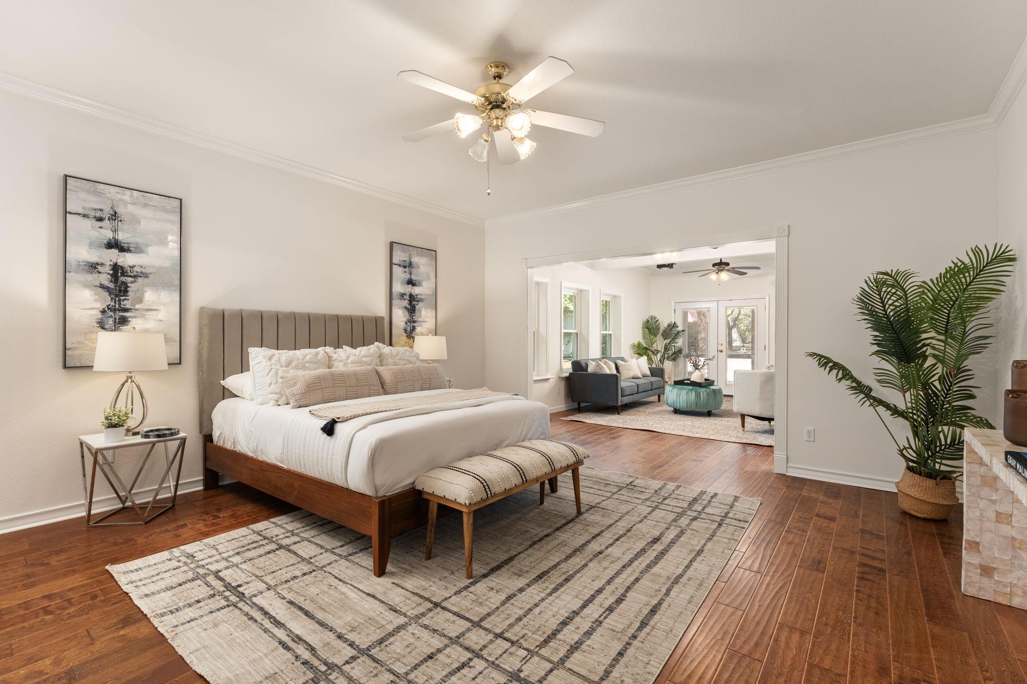 Staged bedroom with a large upholstered bed, hardwood floors, and an opening to a sitting room.