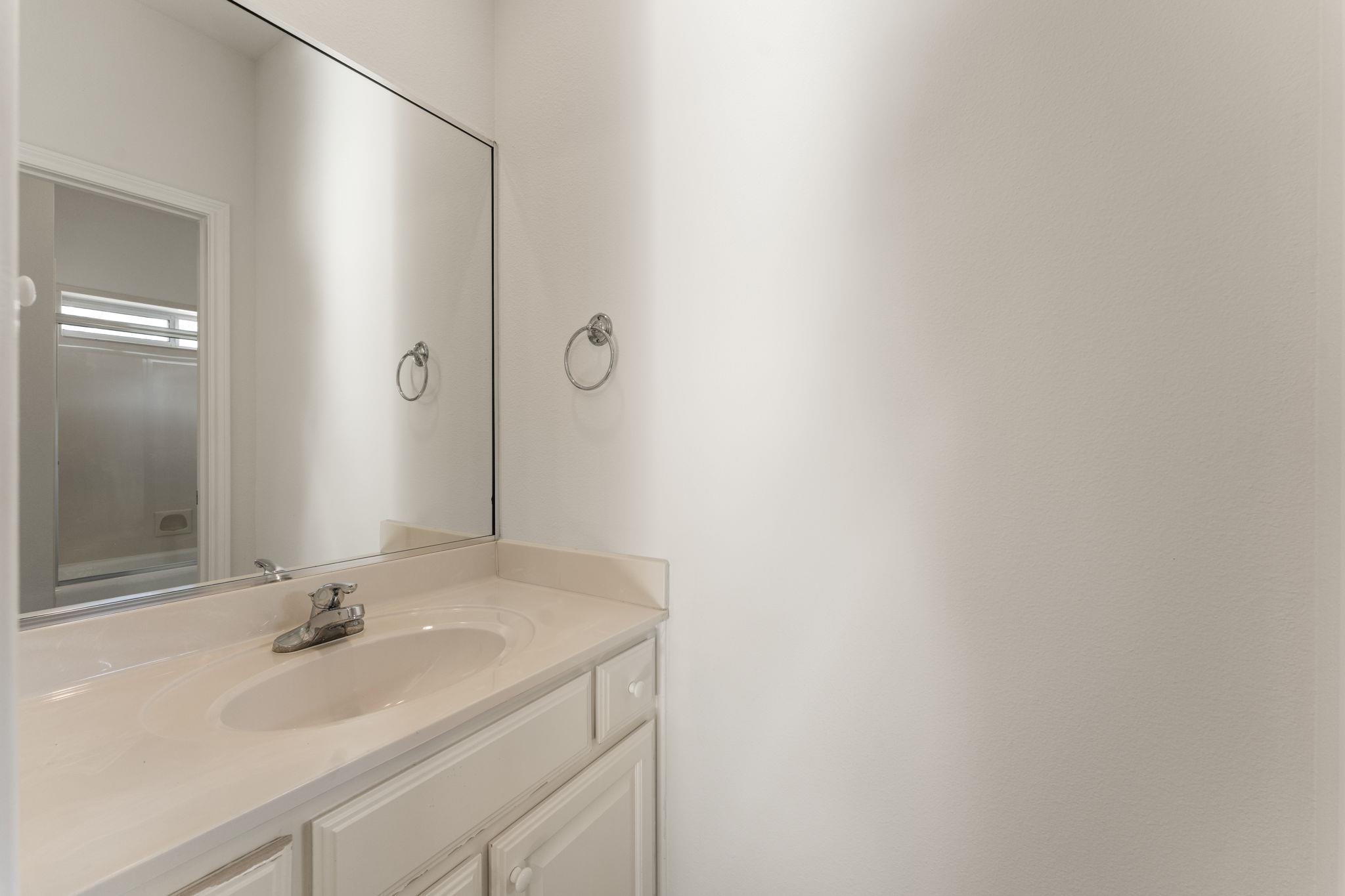 Bathroom vanity with an oval sink, chrome faucet, and large mirror.