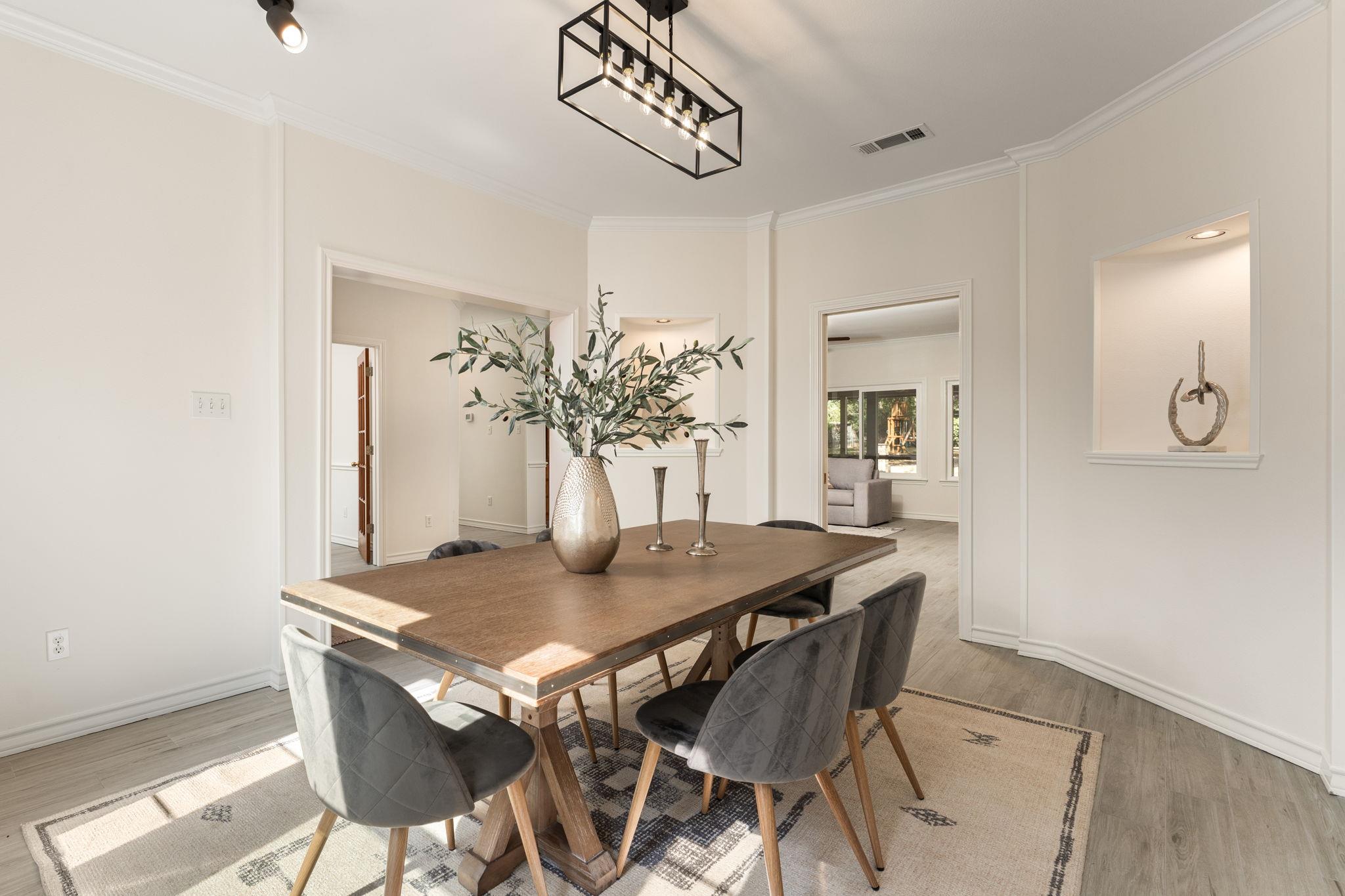 Dining room with a wooden table, gray chairs, geometric rug, and black rectangular chandelier.