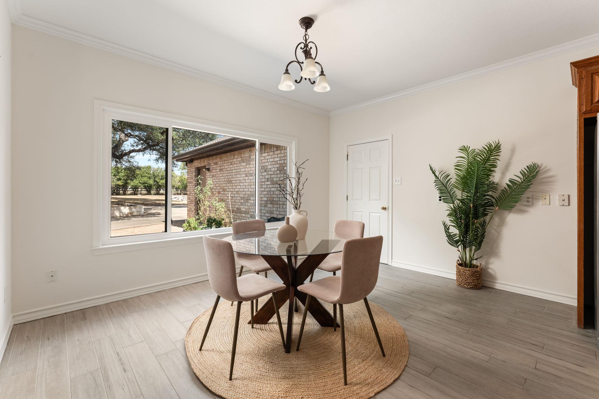 Dining area with a round glass table and four upholstered chairs beside a large window.