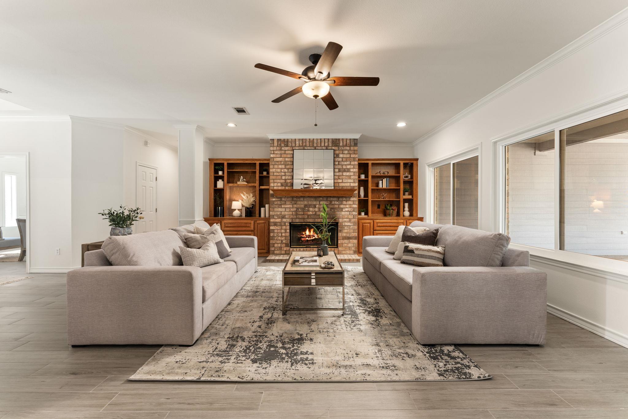 Staged living room with a brick fireplace, built-in shelves, and two sofas facing each other.