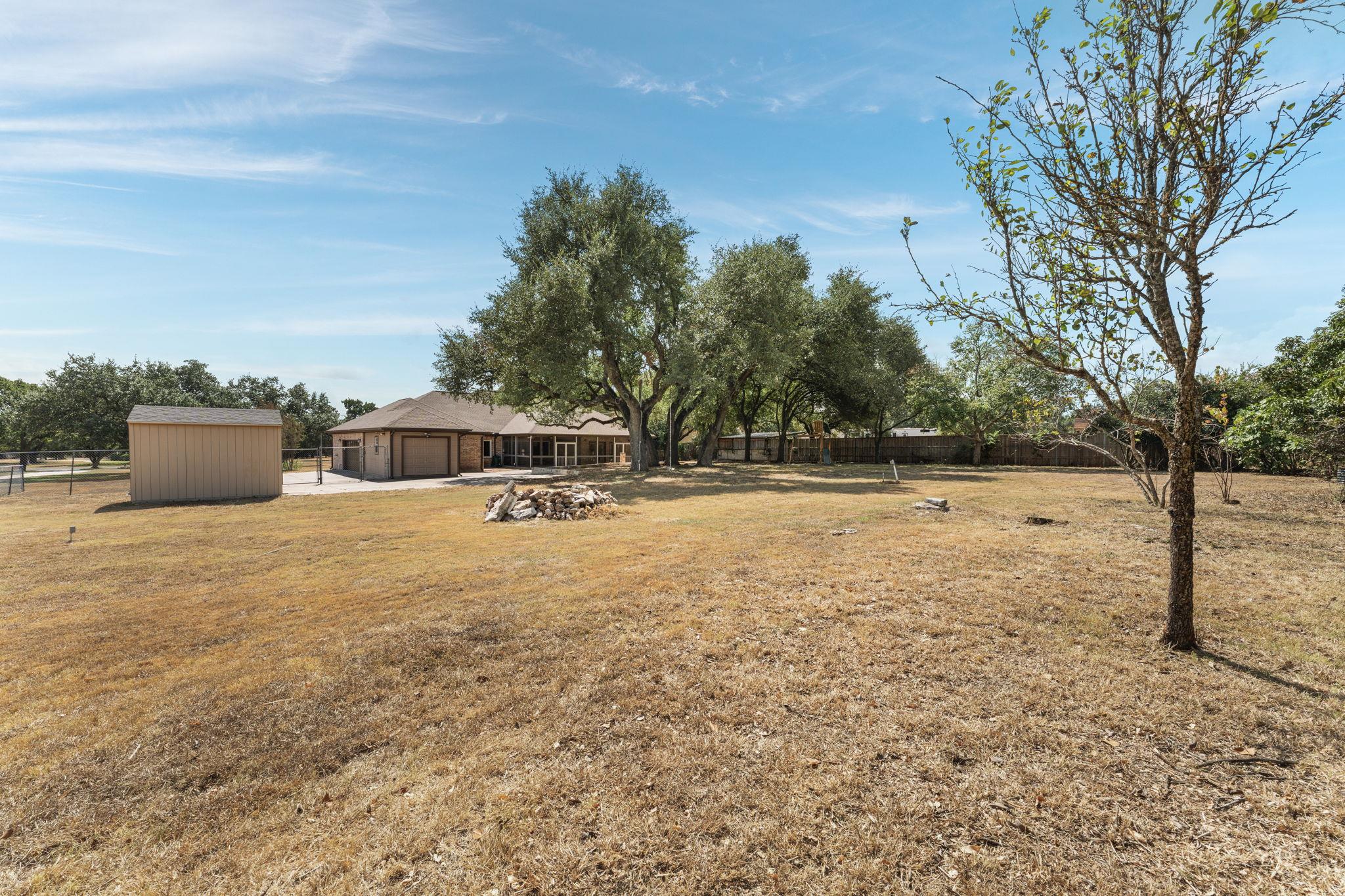 Backyard with a dry lawn, mature trees, storage shed, and a single-story house.