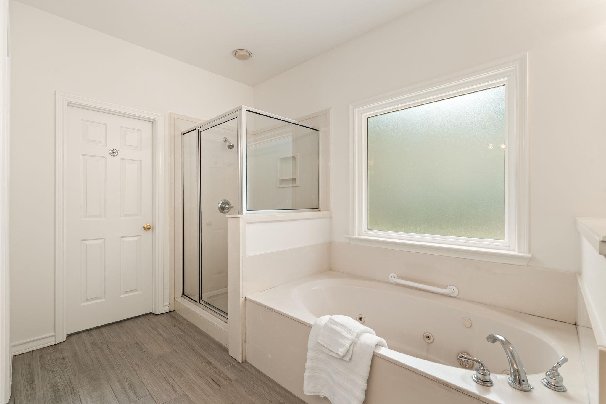 Bathroom with a built-in soaking tub, glass-enclosed shower, and frosted window.