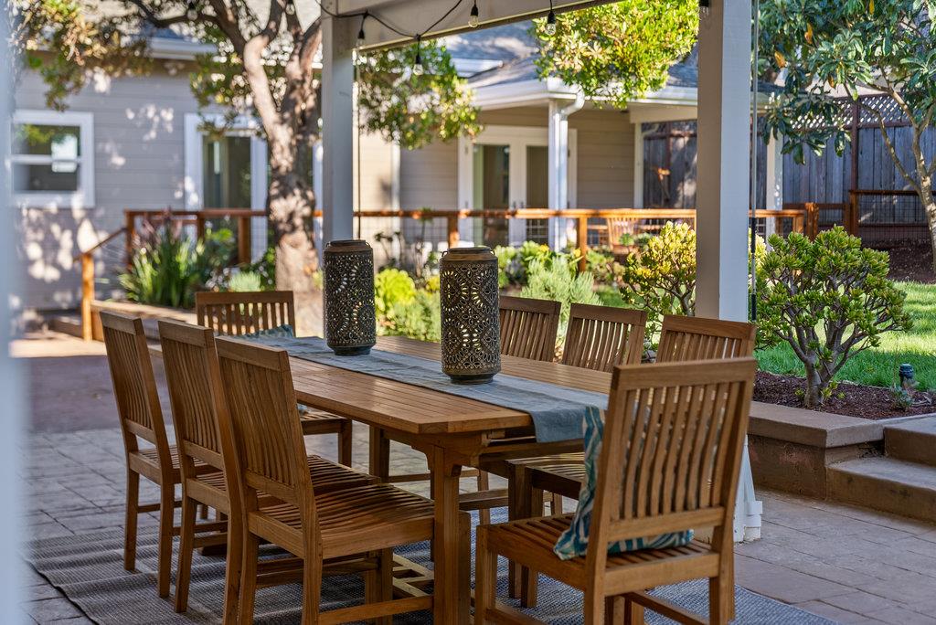 Covered patio with a wooden dining table and chairs beside a landscaped garden.