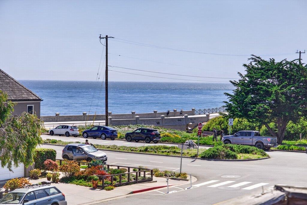 Ocean view beyond a coastal road and seawall, seen over landscaped grounds.